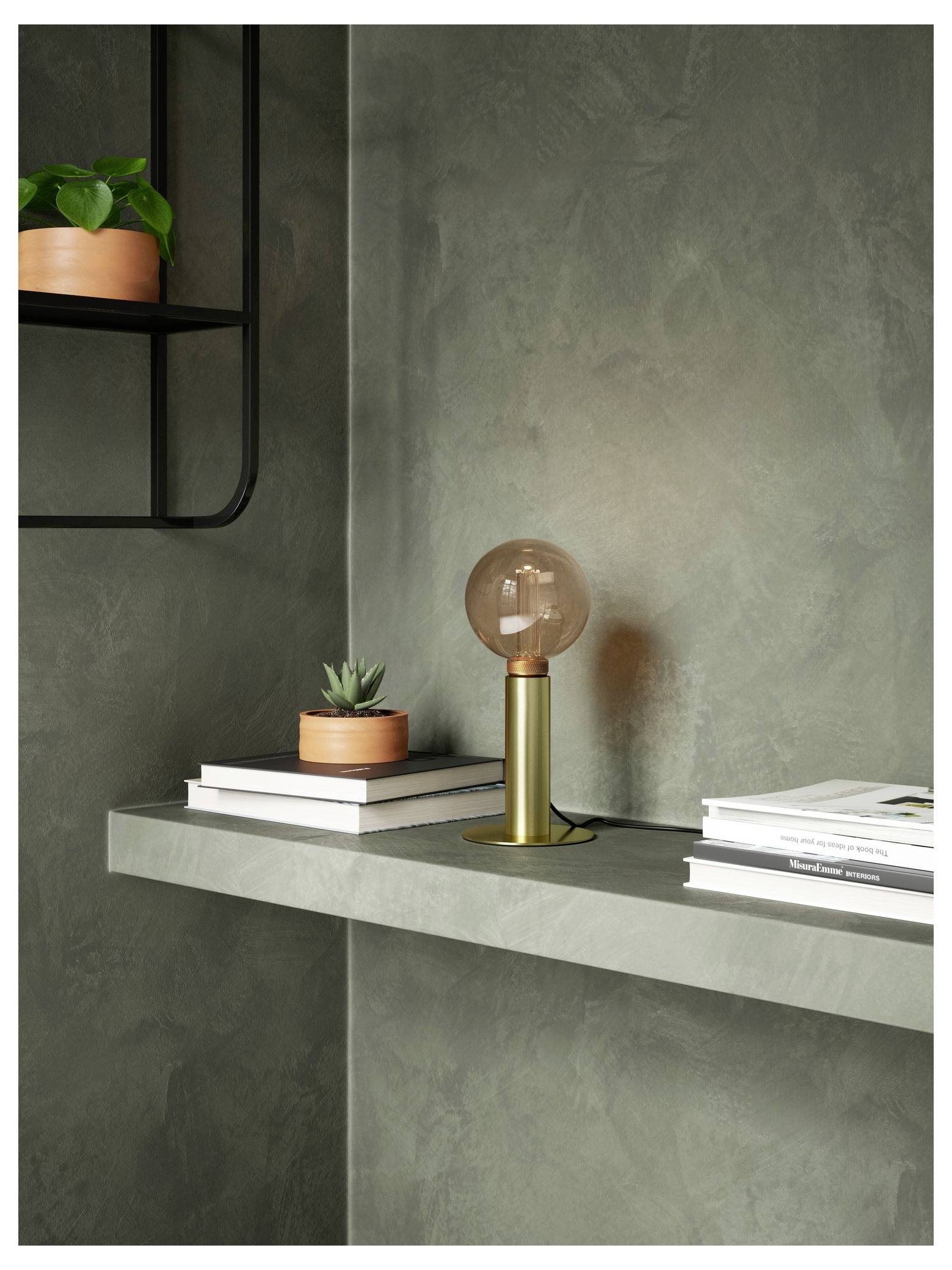 Ein minimalistisches Regal mit einer Globusleuchte, Büchern und kleinen Topfpflanzen vor einer strukturierten grauen Wand.