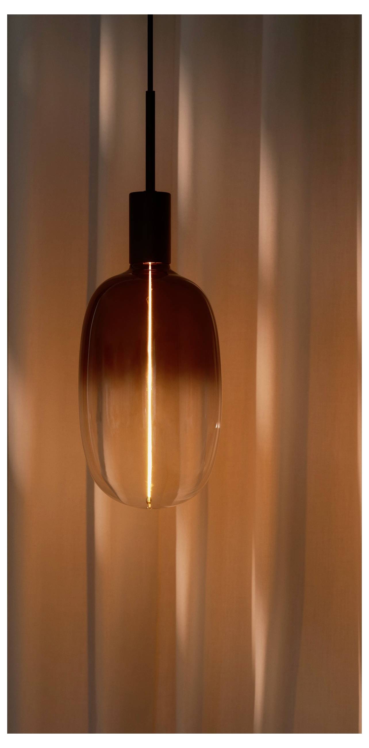 Eine hängende Pendelleuchte aus Bernsteinglas wirft einen warmen Glanz gegen einen weich strukturierten Hintergrund und schafft eine gemütliche und einladende Atmosphäre.