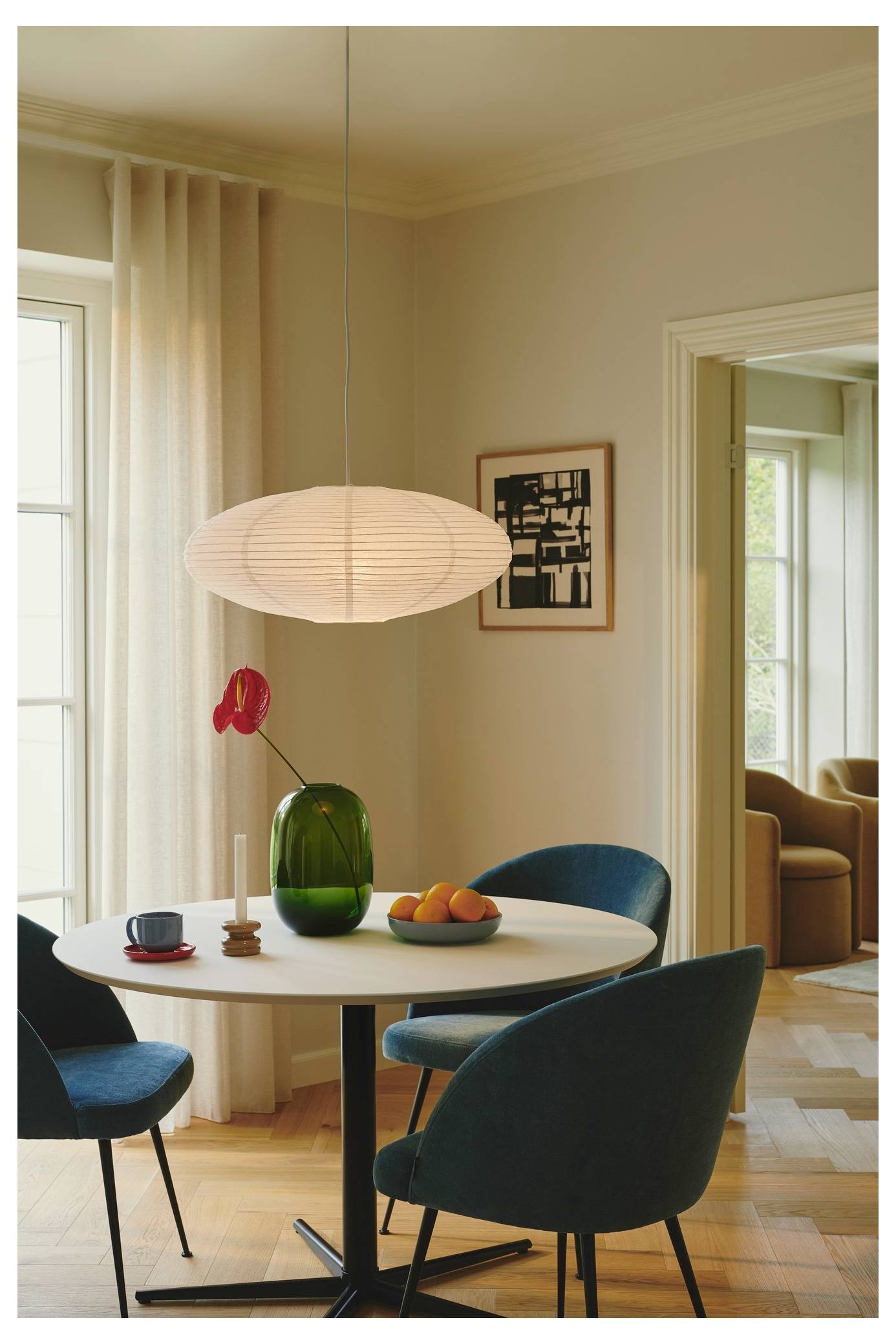 Ein modernes Esszimmer mit einem runden Tisch, vier blauen Stühlen und einer grünen Vase mit einer roten Blume. Eine Pendelleuchte hängt darüber.