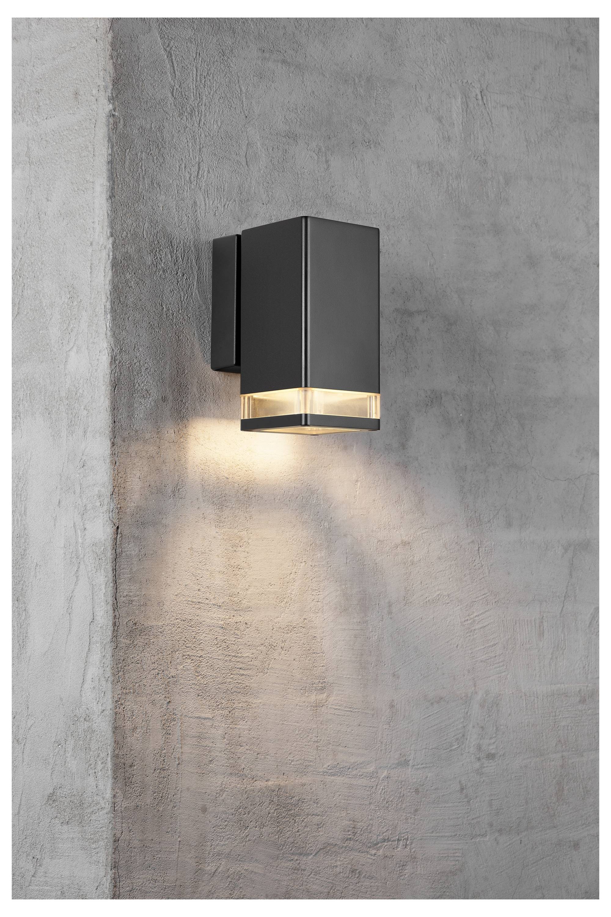 Eine moderne, schwarze, rechteckige wandmontierte Leuchte an einer Betonwand, die einen warmen Glanz nach unten wirft und die darunter liegende Oberfläche beleuchtet.