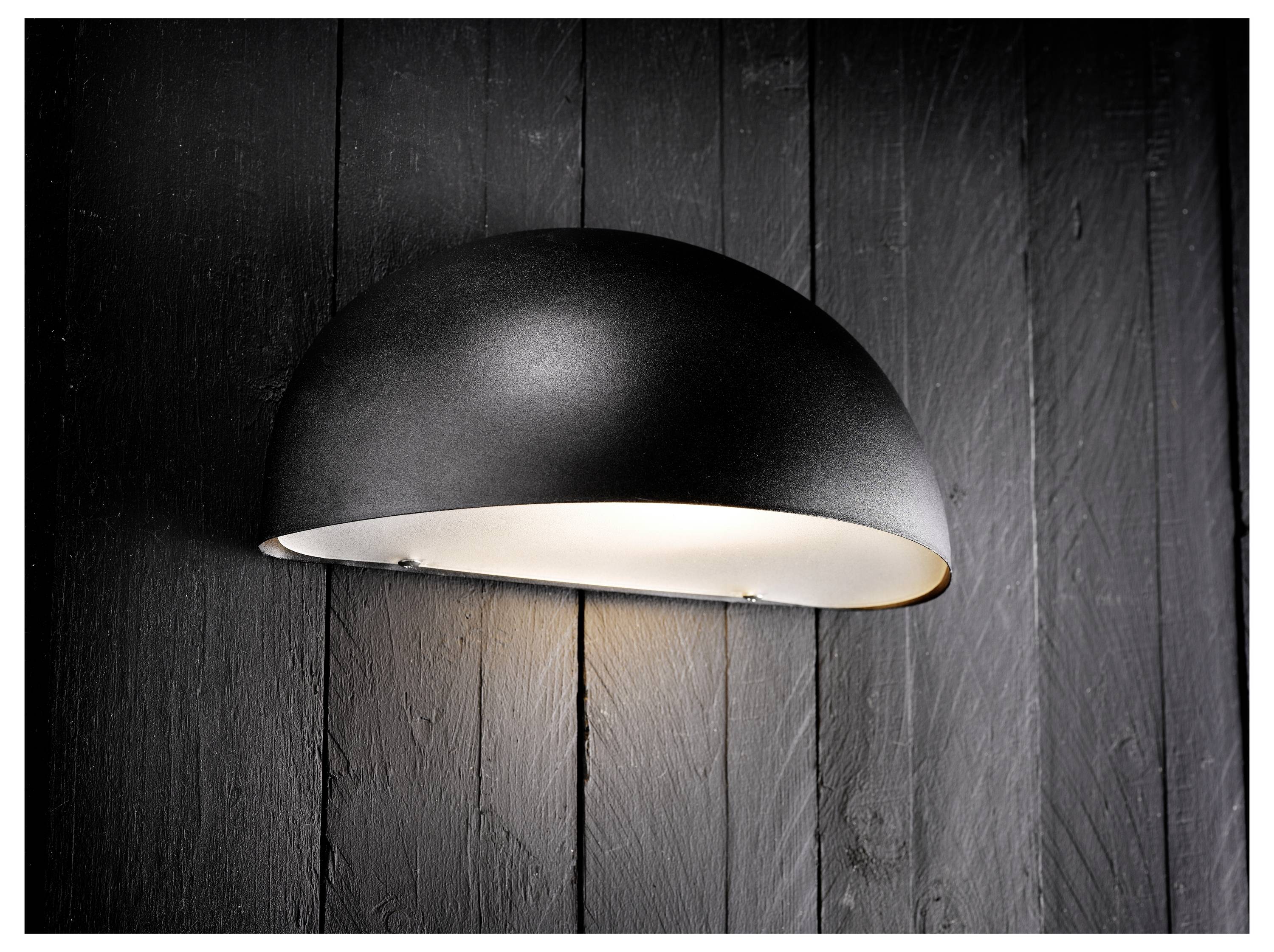 Eine schwarze Halbkuppel-Wandleuchte wirft ein weiches, warmes Licht gegen eine dunkle Holzplanken-Wand und schafft eine gemütliche und moderne Atmosphäre.