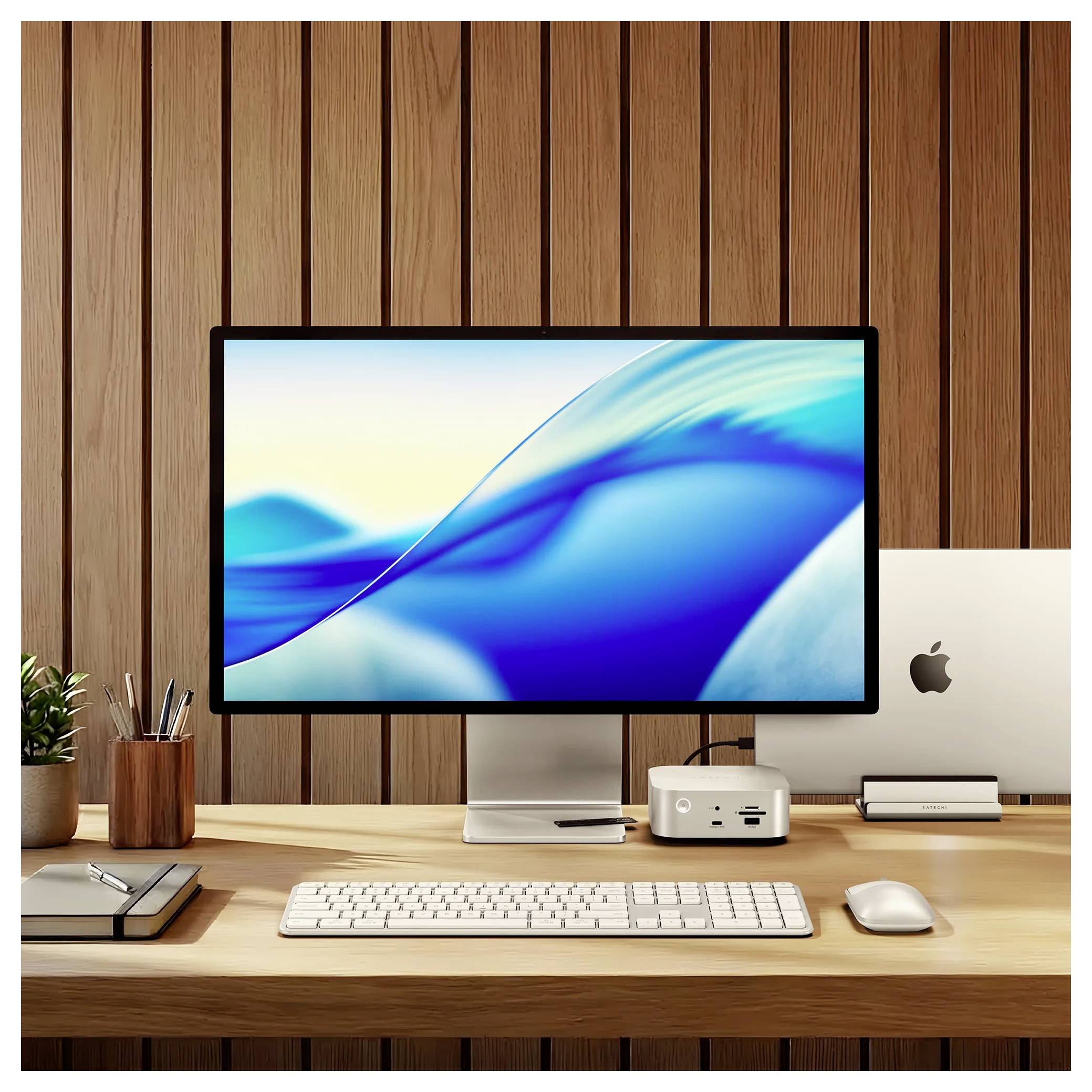 Modernes Schreibtisch-Setup mit einem großen Monitor, der blaue abstrakte Wellen anzeigt, ein Apple-Computer, Tastatur, Maus und Zubehör vor einer holzgetäfelten Wand.