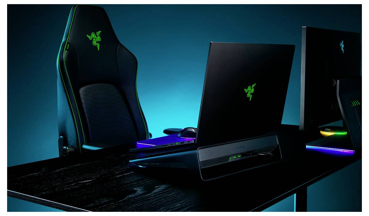 Ein Gaming-Setup mit einem eleganten schwarzen Laptop mit leuchtendem grünem Logo, begleitet von einem Gaming-Stuhl und farbig beleuchteten Zubehörteilen.
