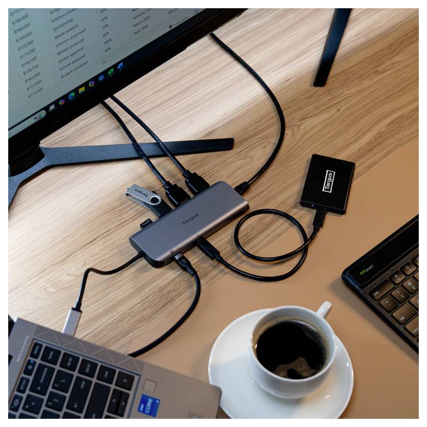 Arbeitsplatzeinrichtung mit mehreren Geräten, einschließlich Laptops, die über einen Hub verbunden sind, mit einer Kaffeetasse in der Nähe auf einem Holzschreibtisch.