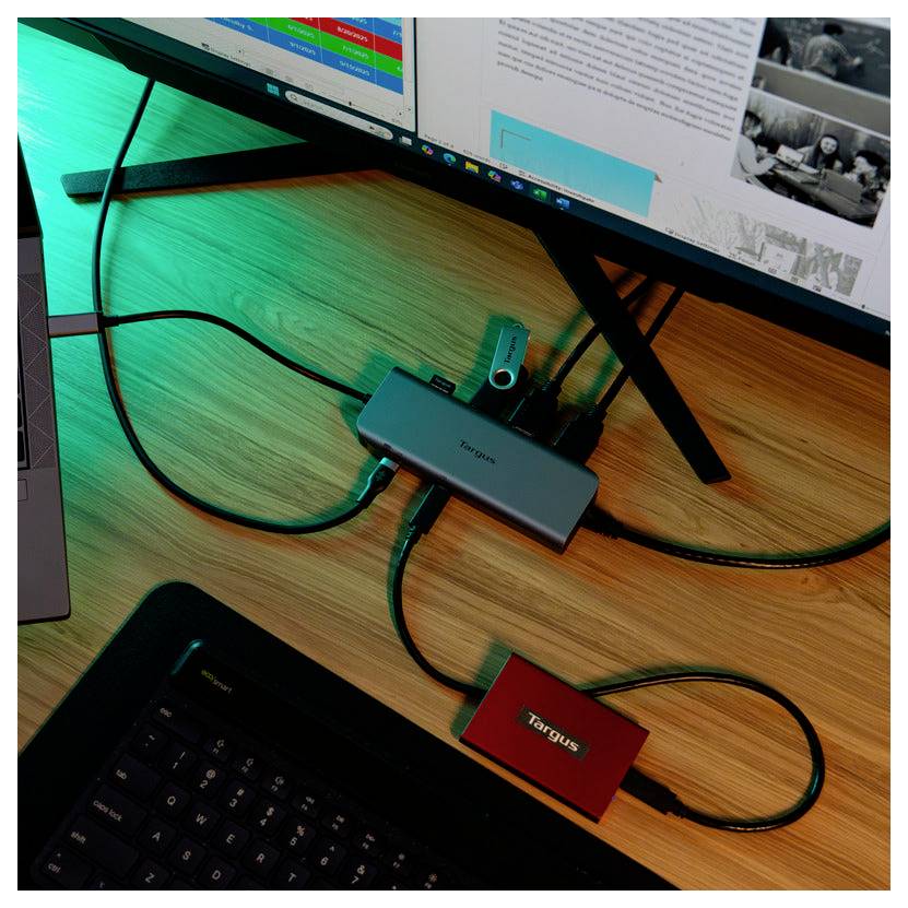 Ein Schreibtisch-Setup mit einem Computermonitor, einem USB-Hub mit mehreren Anschlüssen und einer Targus-Festplatte, alles auf einer Holzoberfläche.