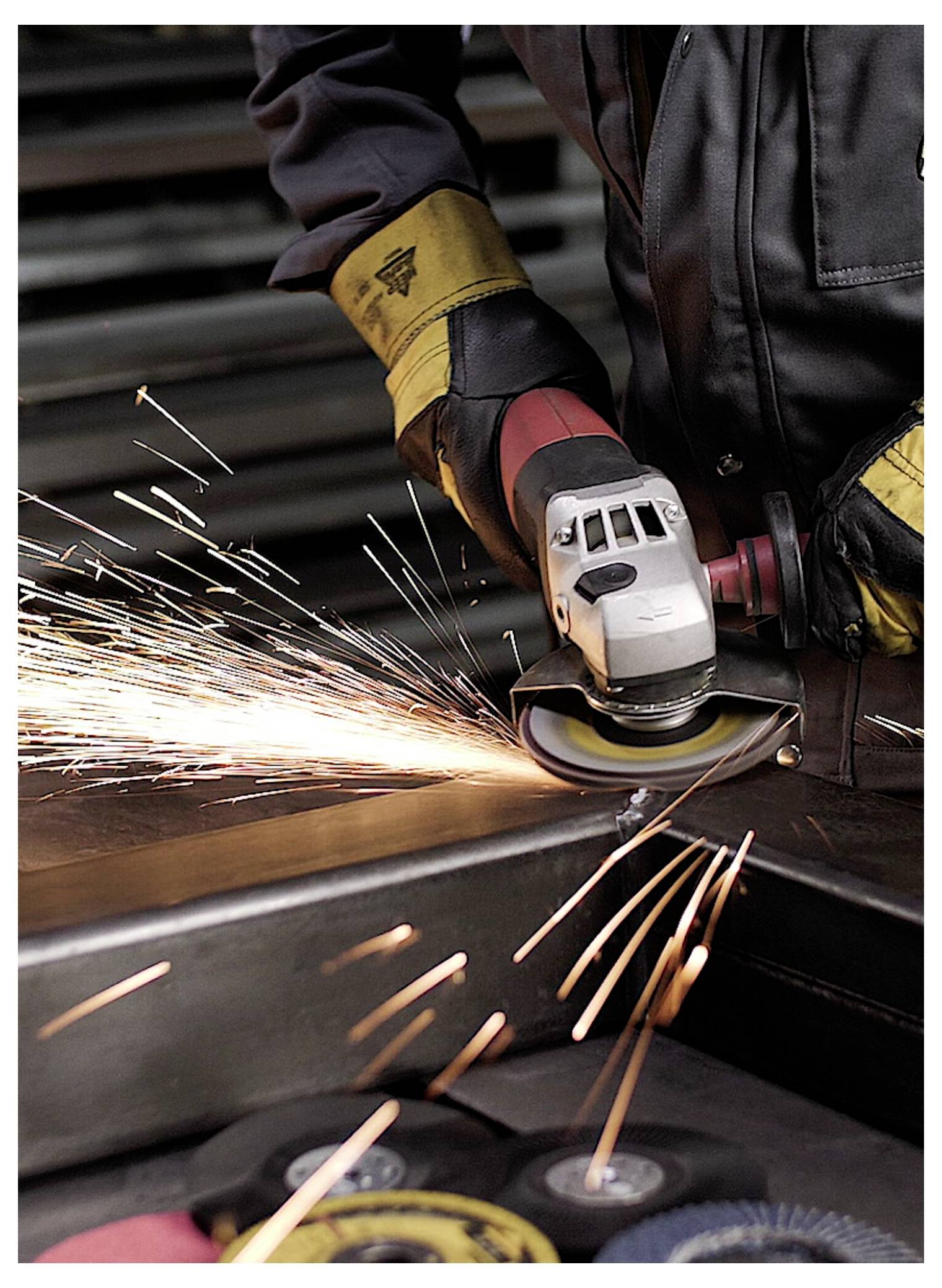 Eine Person in Schutzausrüstung nutzt einen Schleifer, der helle Funken ausstößt, auf einer Metalloberfläche, was auf Metallverarbeitung oder industrielle Aktivität hindeutet.