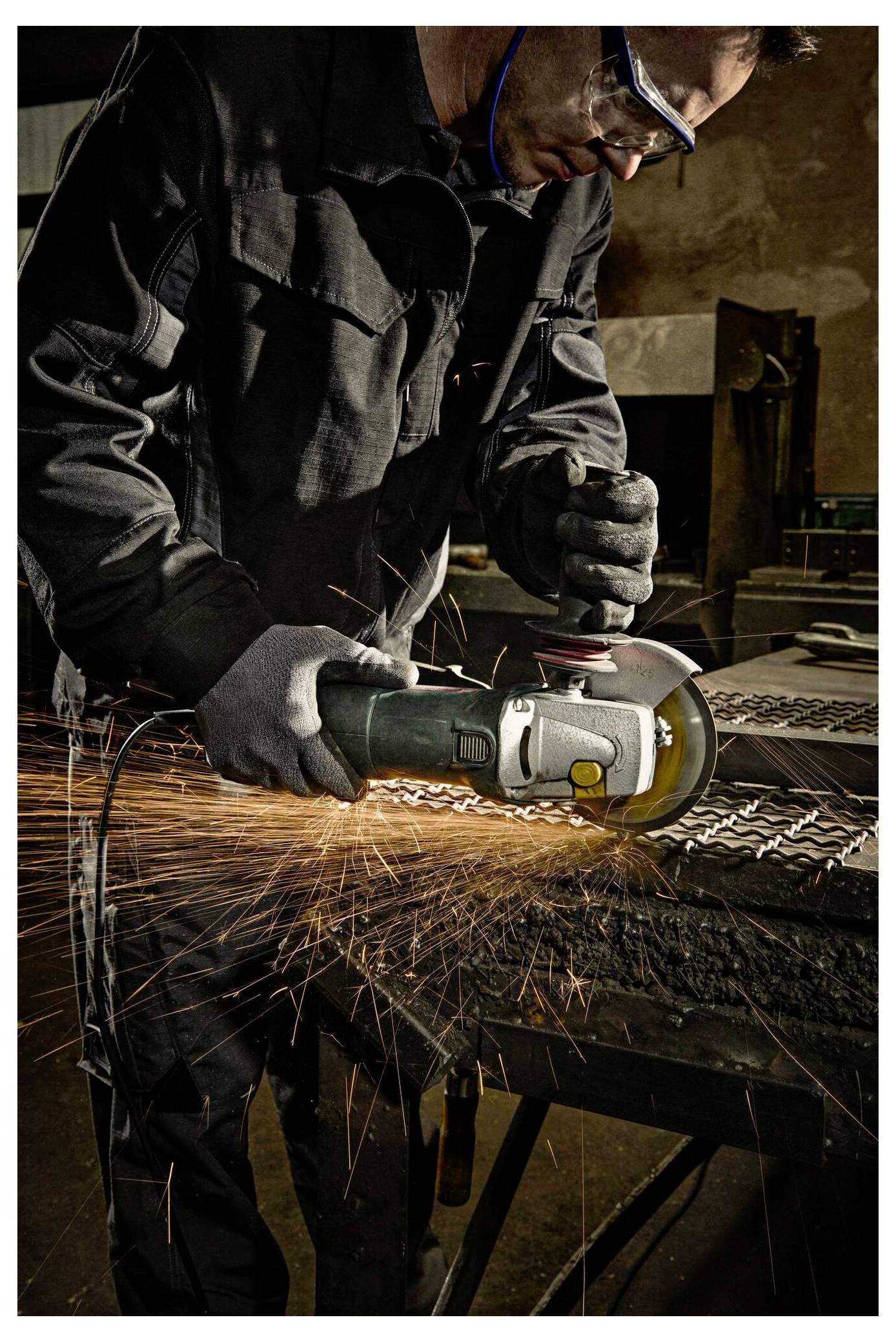 Eine Person in Schutzausrüstung verwendet einen Winkelschleifer auf einer Metalloberfläche und erzeugt dabei Funken.