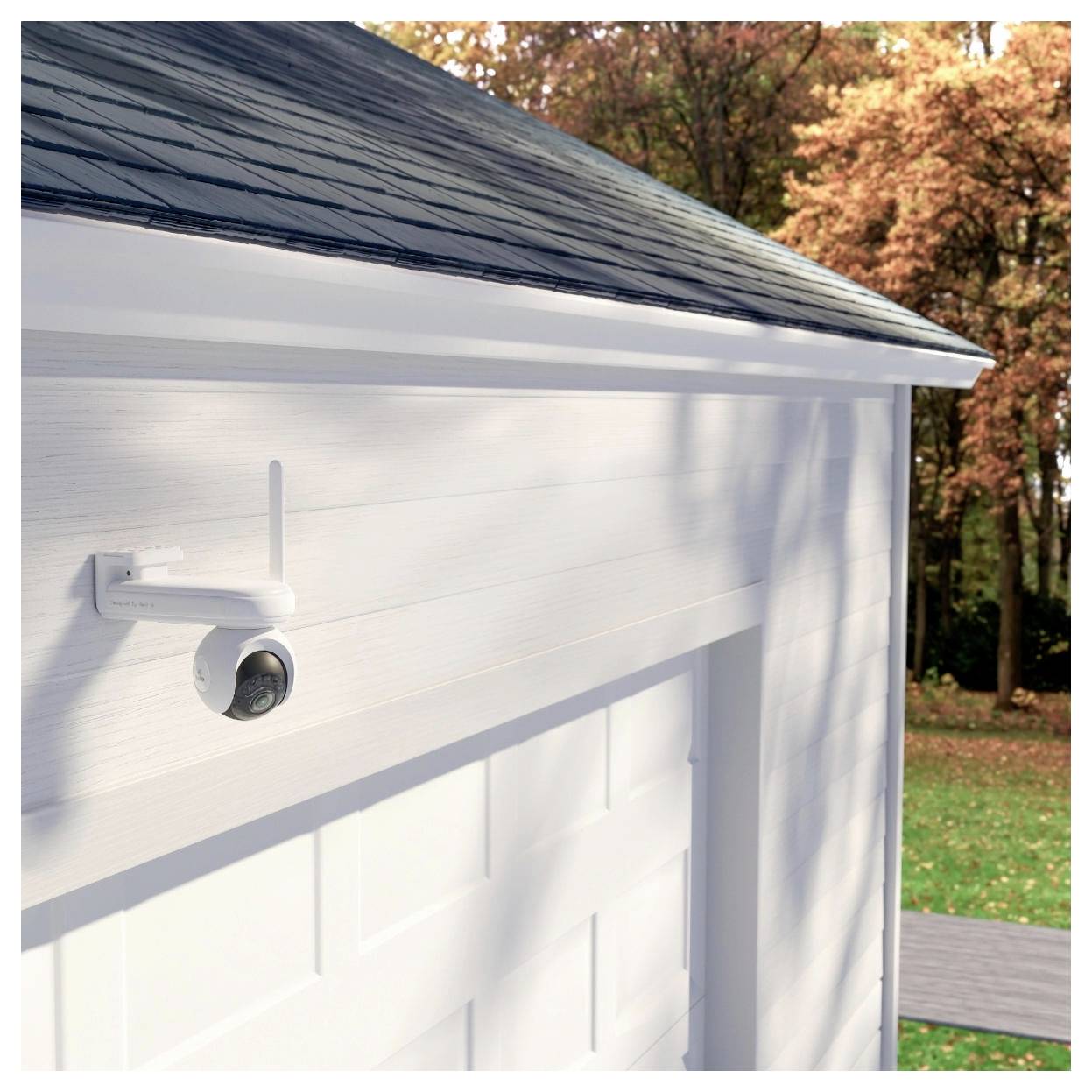 Eine weiße Garage mit einer Sicherheitskamera, die an der Ecke angebracht ist, umgeben von Herbstbäumen.