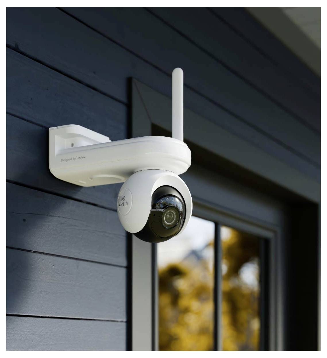 Eine Sicherheitskamera ist an der Außenseite eines dunkelgestrichen Gebäudes montiert, positioniert in der Nähe eines Fensters, das Bäume widerspiegelt.