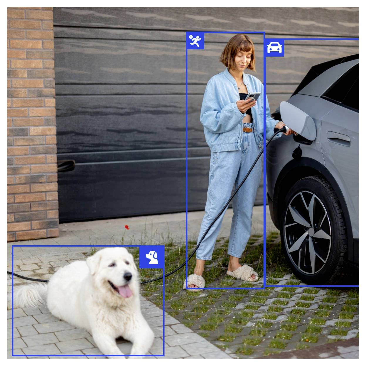 Eine Person in blauer Kleidung lädt ein Elektroauto auf, während sie ein Telefon in der Hand hält. In der Nähe liegt ein flauschiger weißer Hund auf dem Boden.