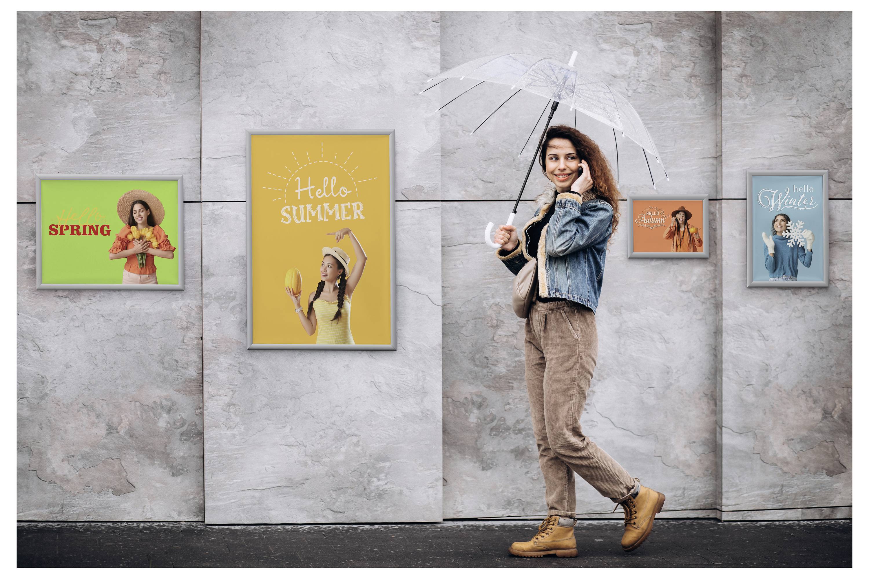 Eine Frau, die einen durchsichtigen Regenschirm hält, geht an einer Wand vorbei, auf der vier Poster mit Jahreszeitenmotiven angebracht sind, die mit 'Hallo Frühling', 'Hallo Sommer' und anderen beschriftet sind.