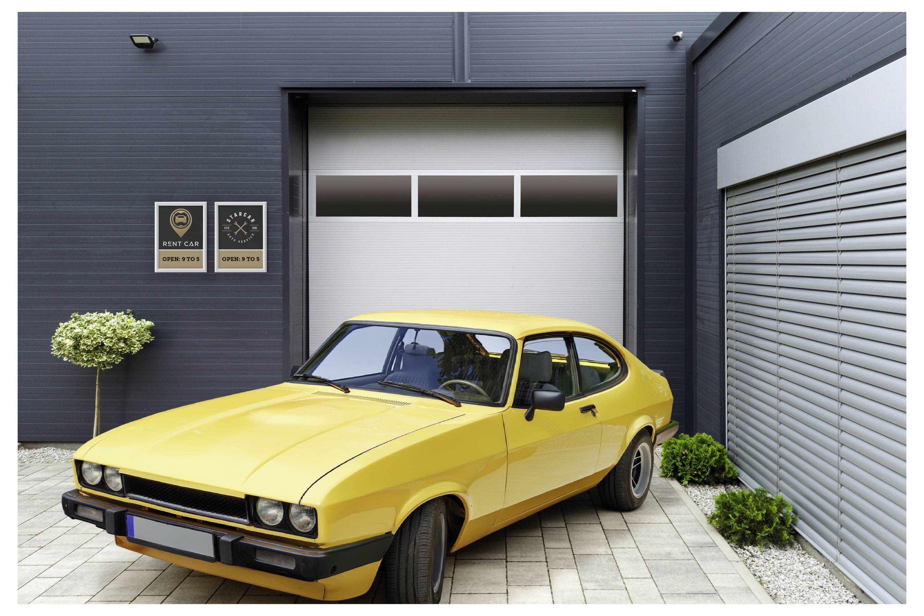 Ein gelbes Vintage-Auto ist auf einer Ziegelestein-Einfahrt vor einer modernen Garage geparkt, mit zwei an der Wand montierten Schildern, die Temperatur und Geschlossenheit anzeigen.