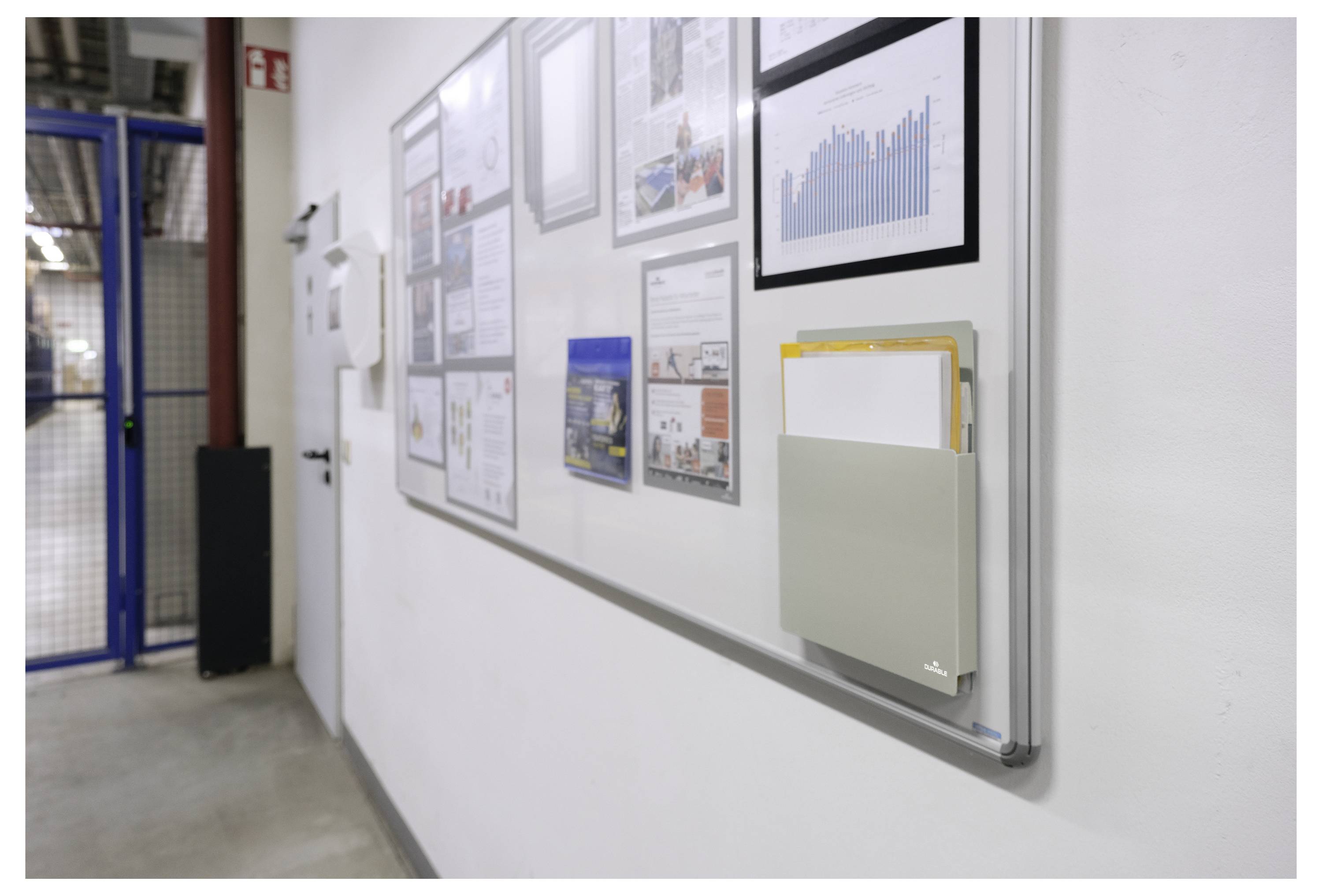 Eine Wand am Arbeitsplatz mit gerahmten Diagrammen, Grafiken und Zertifikaten, einschließlich eines Balkendiagramms und einem Aktenhalter mit Dokumenten.