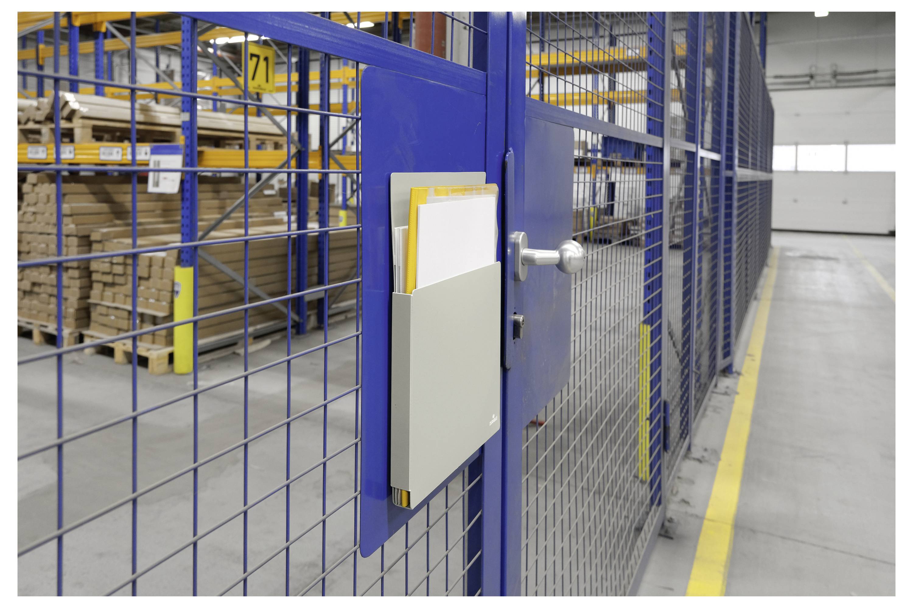 Eine Lagerhausszene mit einem blauen Metalltor, an dem ein Klemmbrett mit Papieren befestigt ist; im Hintergrund sind Stapel von Holzpaletten sichtbar.
