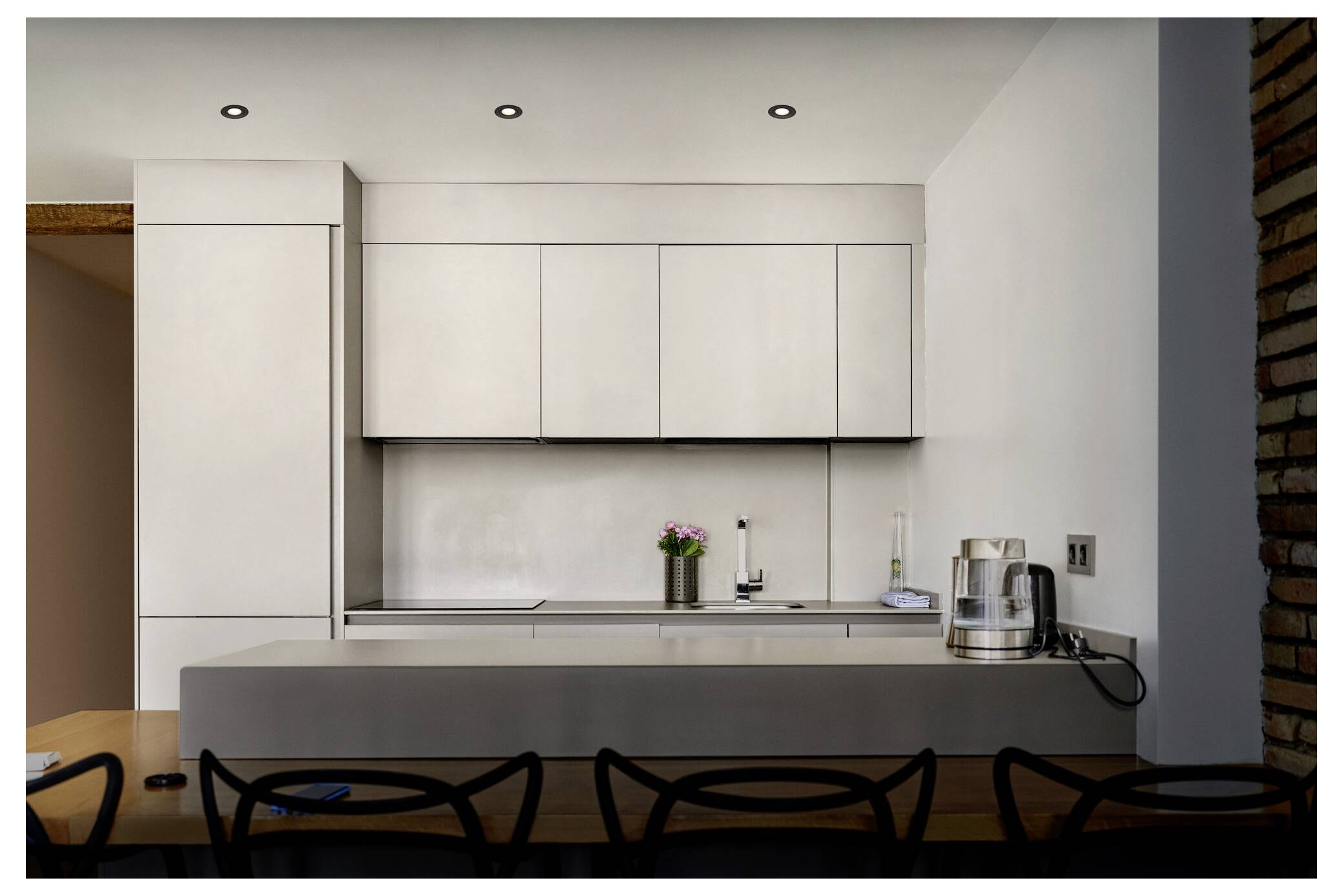 Minimalistische moderne Küche mit eleganten weißen Schränken, einer grauen Arbeitsplatte und eingebauten Geräten. Eine kleine Pflanze und Küchenutensilien sind auf der Arbeitsplatte angeordnet.