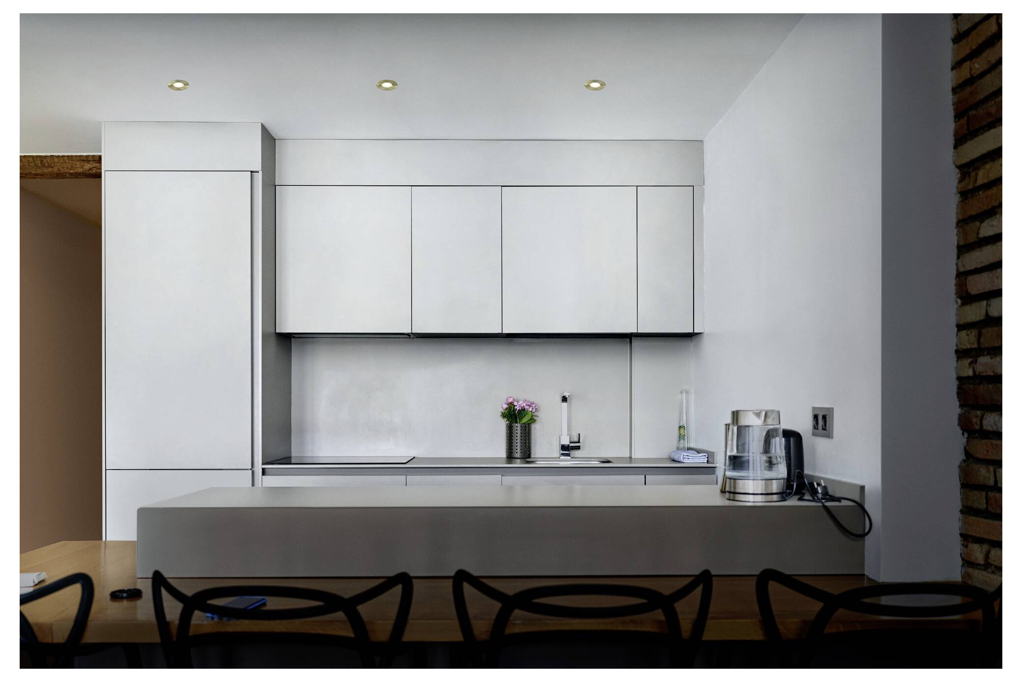 Moderne Küche mit eleganten weißen Schränken, einem Edelstahlwasserkocher und Topfpflanzen auf der Arbeitsplatte. Minimalistisches Design und weiches Licht.