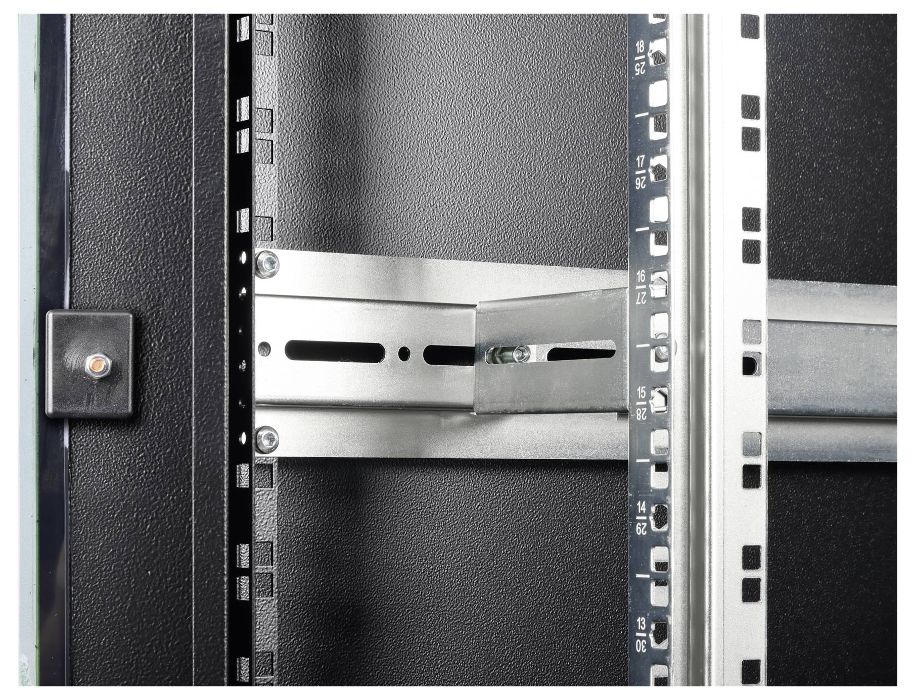 Nahaufnahme eines Metallgestells oder Serverrack-Gehäuses mit detaillierten Montagelöchern und einer Befestigungsklammer auf strukturiertem Untergrund.