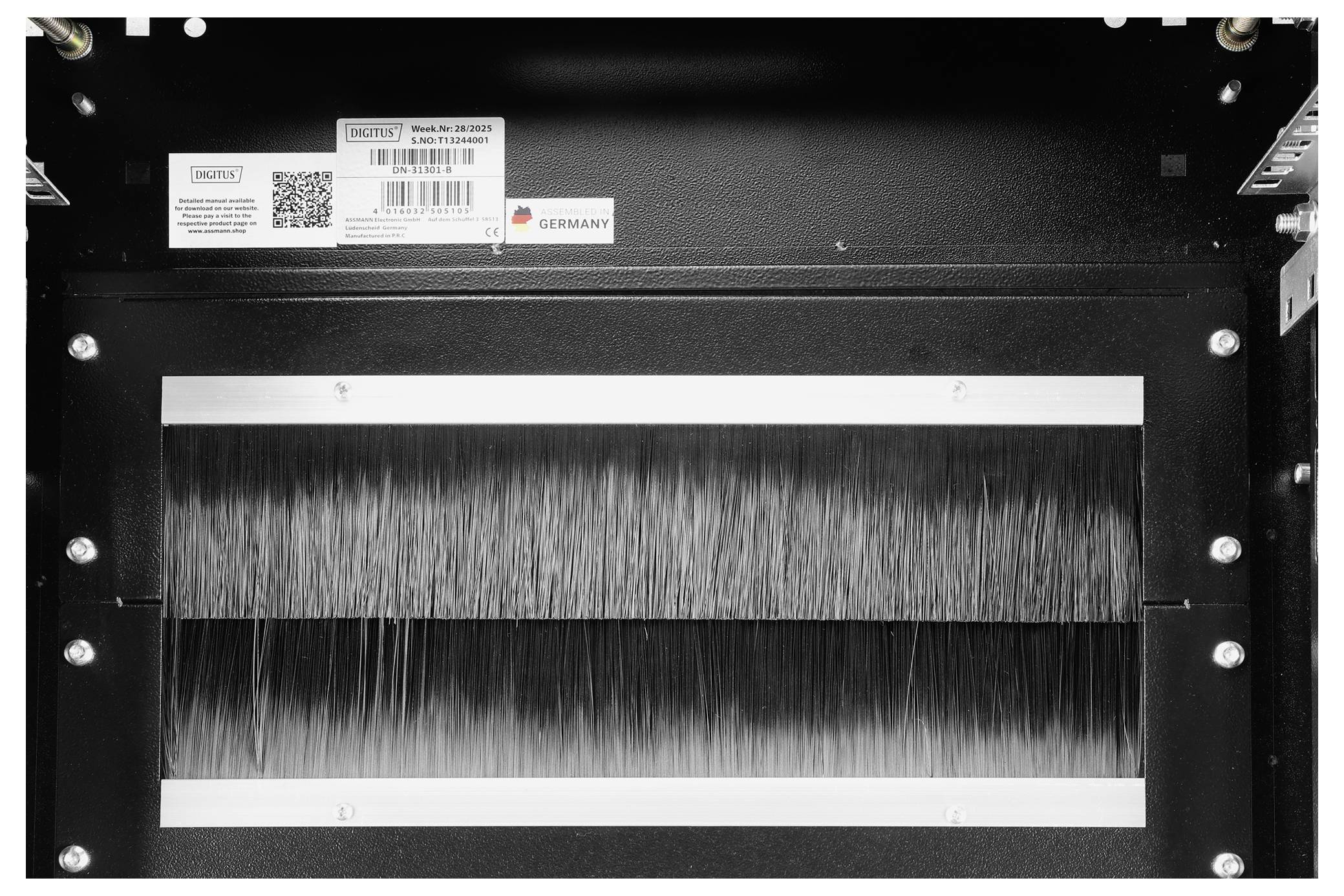 „Innenansicht einer schwarzen Kammer mit Metallbürsten in der Mitte, umgeben von einem Metallrahmen. Etiketten und ein Barcode sind oben sichtbar.