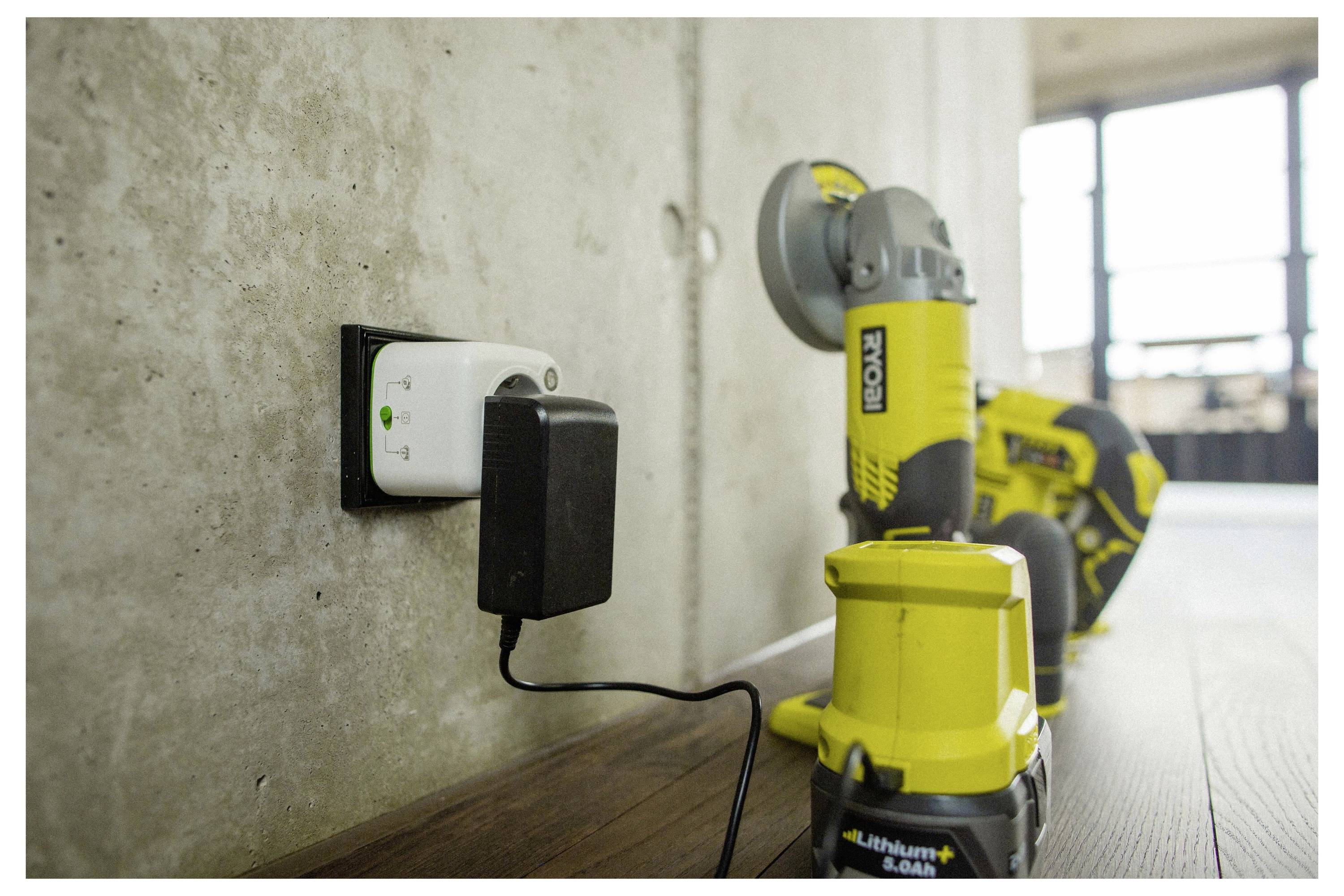 Ein eingestecktes Elektrowerkzeug-Ladegerät mit einem gelb-schwarzen kabellosen Bohrschrauber und einer Handkreissäge auf einem Holzboden vor einer Betonwand.