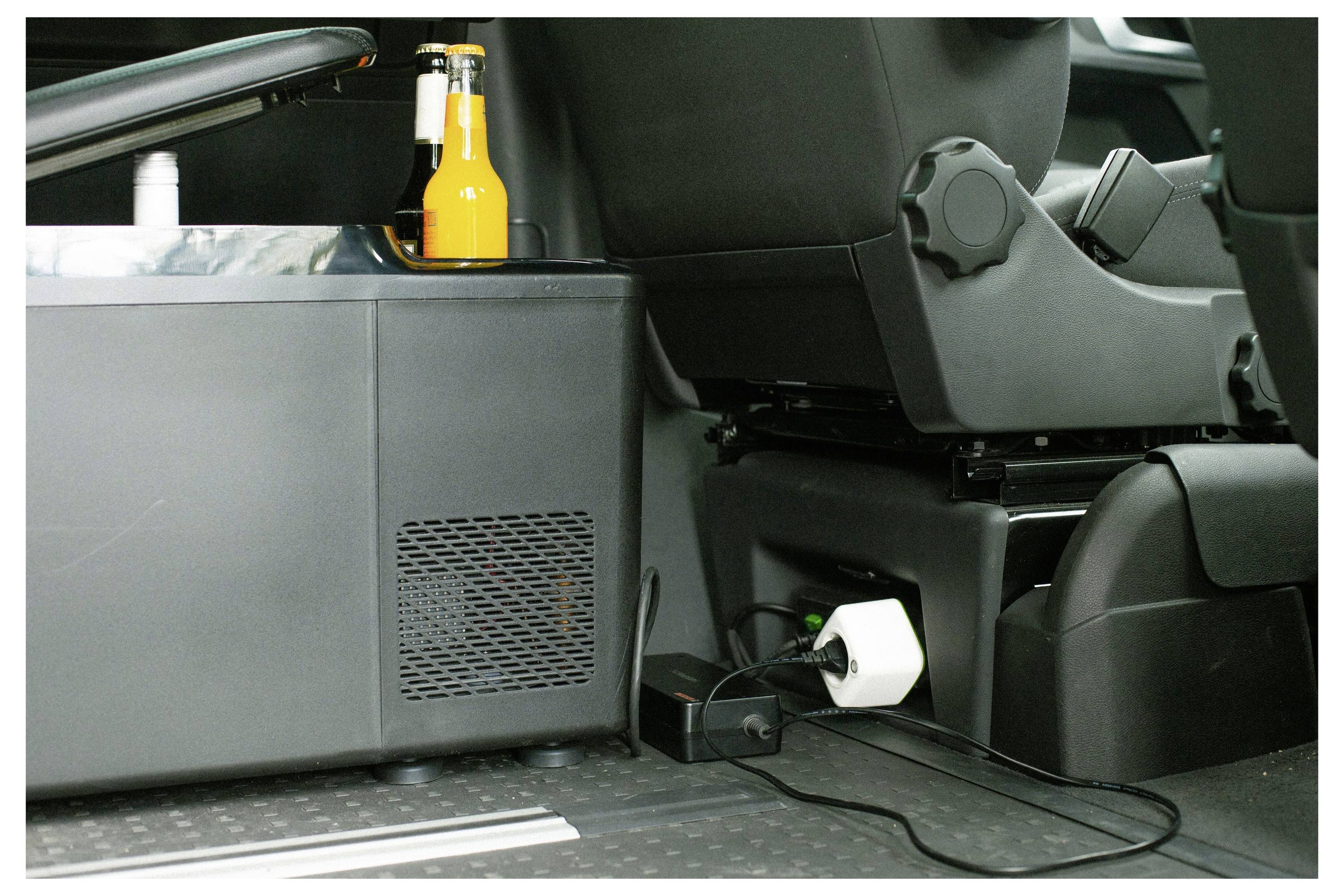 In einem Fahrzeug steht ein kleiner Kühlschrank auf dem Boden neben der Rückbank und lagert zwei abgefüllte Getränke oben drauf.