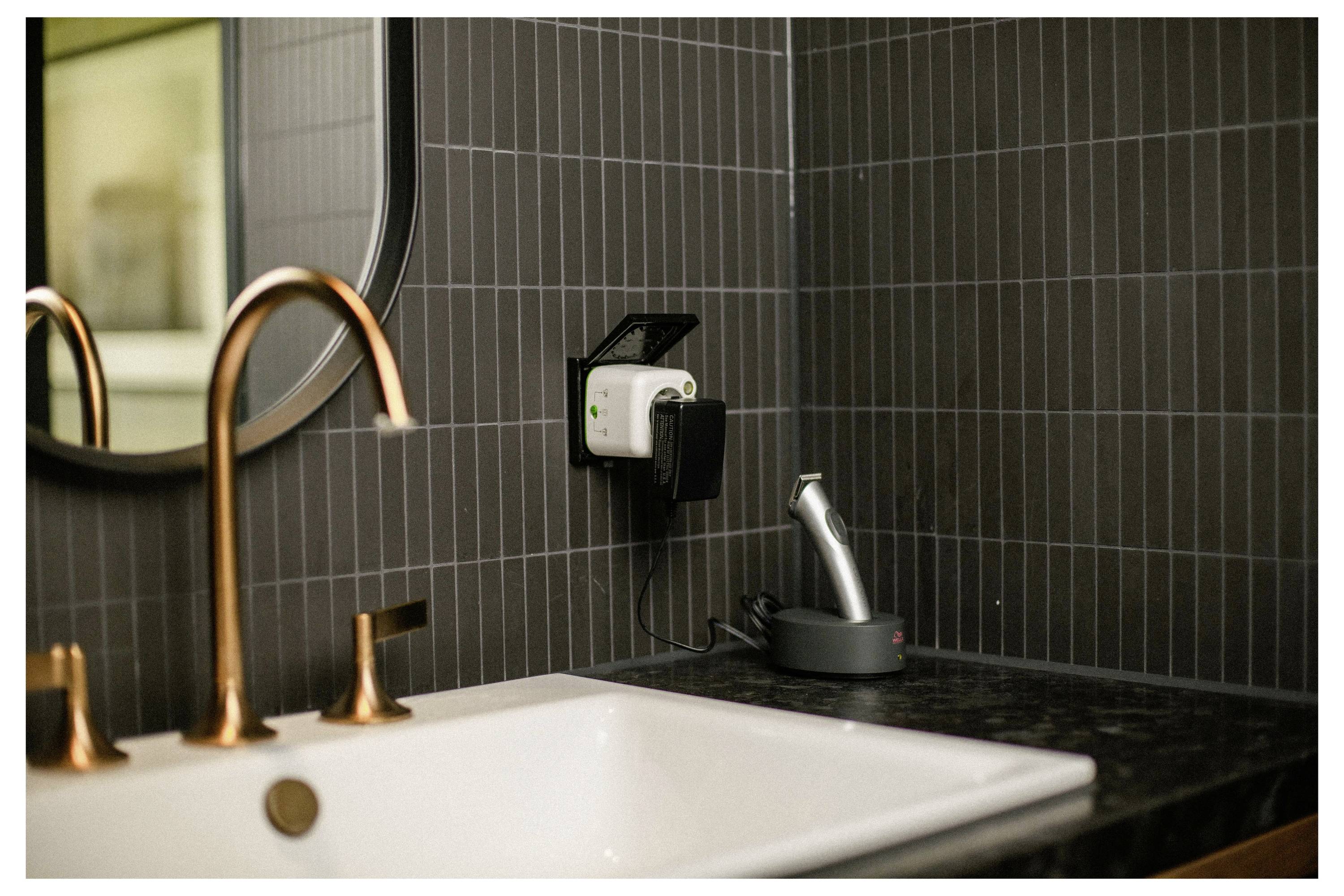 Ein modernes Badezimmerbecken mit rosé-goldfarbenen Armaturen und einer schwarzen Arbeitsplatte. Ein Zahnbürstenladegerät und ein angeschlossenes Gerät stehen auf der Arbeitsplatte.