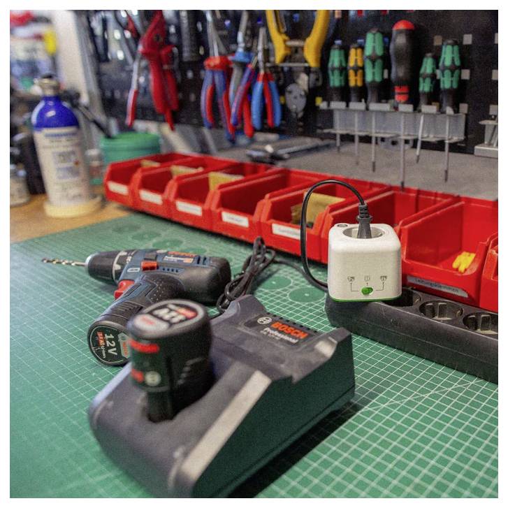 „Eine Werkstattbank mit einem angeschlossenen Akkuladegerät, einer Akkubohrmaschine mit einem zweiten Akku und einem organisierten Werkzeugständer im Hintergrund.