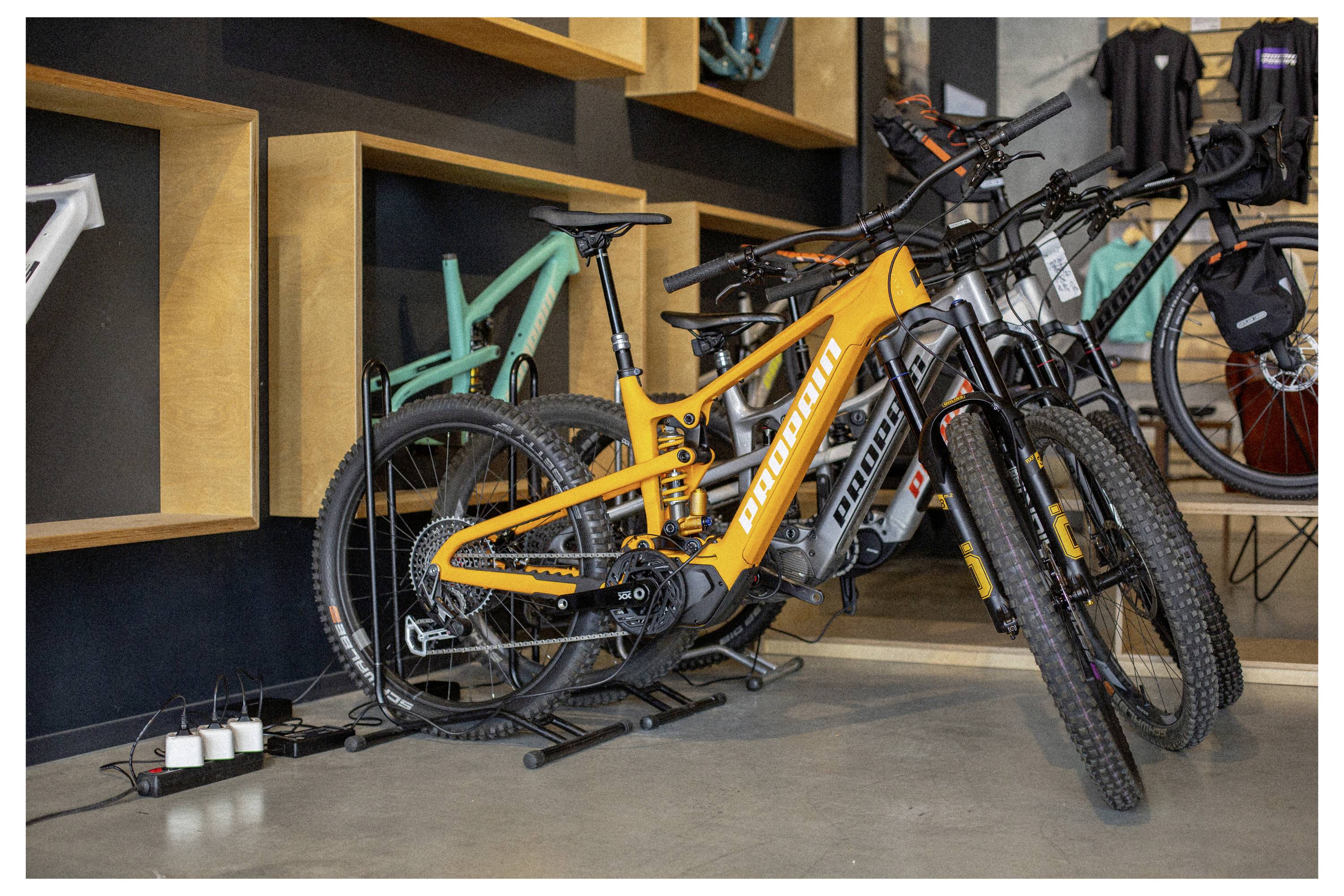 Orange-E-Bike, das auf einem Ausstellungsflur ausgestellt ist, umgeben von anderen Fahrrädern, mit Fokus auf sein elegantes Design und seine lebendige Farbe.