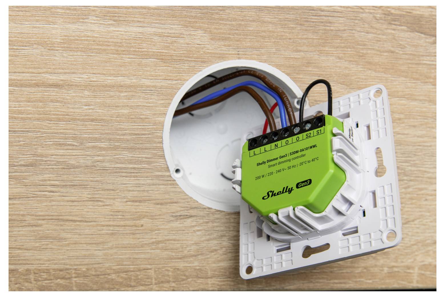 Ein elektrischer Schalter mit freiliegenden Kabeln, auf einer Holzoberfläche montiert. Der Schalter ist mit „Shelly Pro