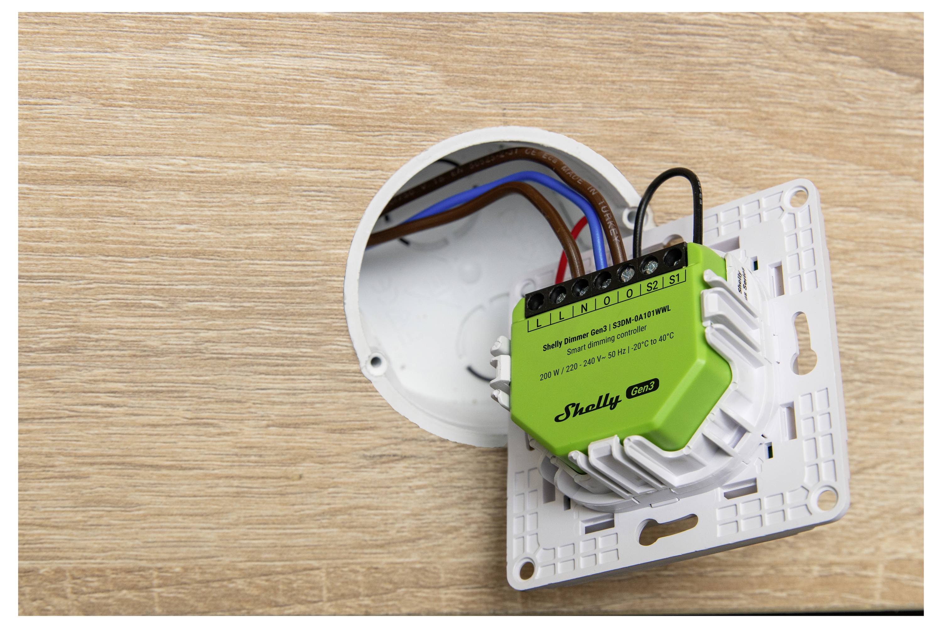 Ein grüner intelligenter Schalter mit Kabeln wird teilweise in eine Wandsteckdose gegen eine Holzoberfläche eingeführt und zeigt eine Hausautomationsinstallation.