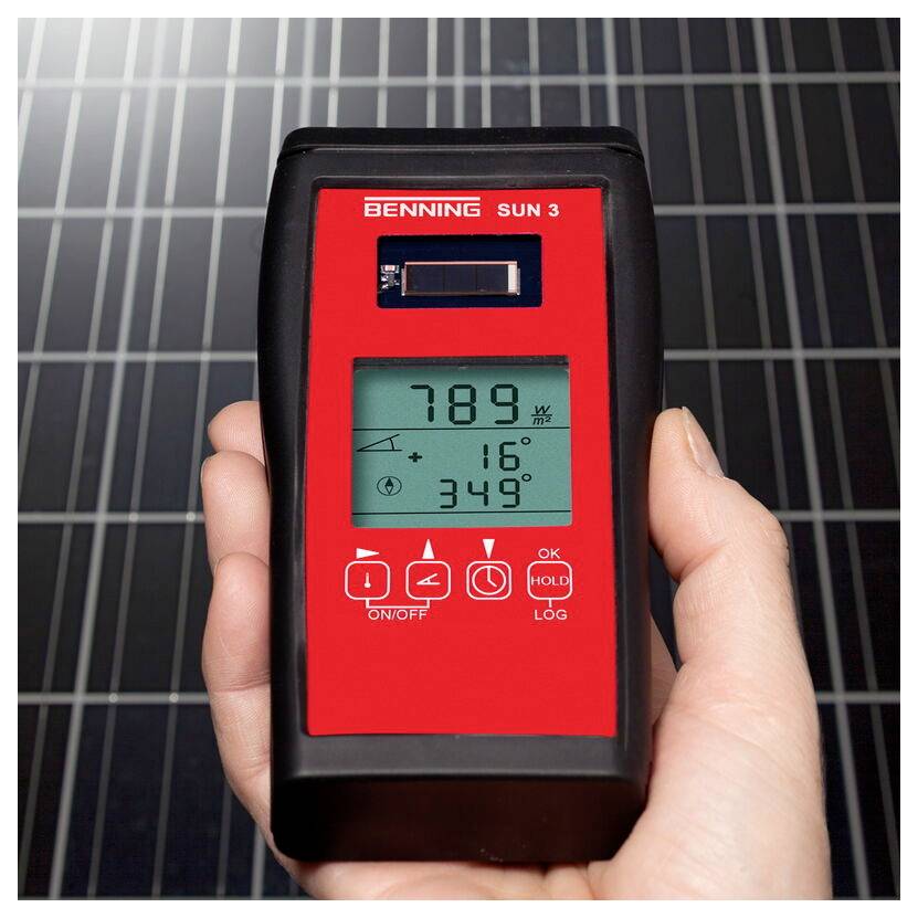 Eine Hand hält ein digitales Sonneneinstrahlung-Messinstrument, das 789 W/m², 16°C, 349° anzeigt. Solarpanele sind im Hintergrund sichtbar.