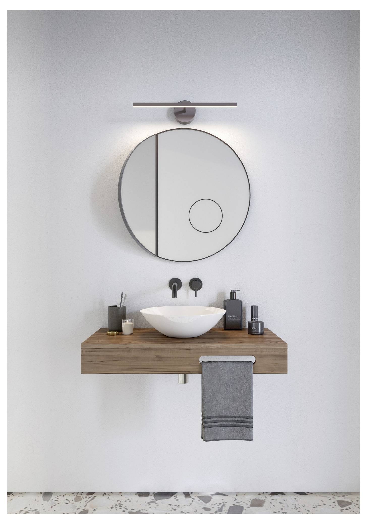 Ein modernes Badezimmerwaschtisch mit rundem Spiegel, Holzplatte, weißem Waschbecken und schlankem Wasserhahn. Toilettenartikel und ein graues Handtuch sind ordentlich angeordnet.