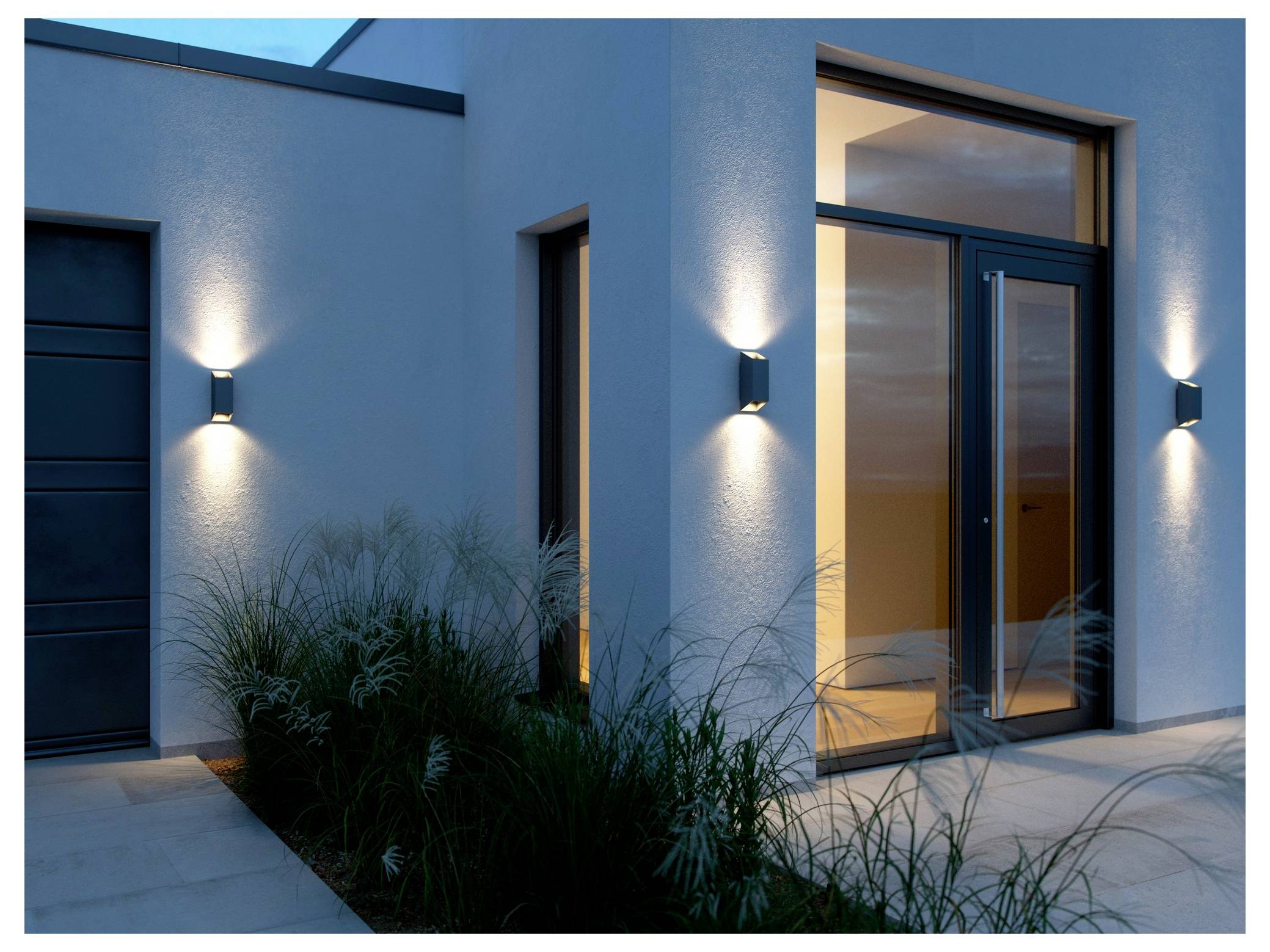 Ein moderner Hauseingang in der Abenddämmerung mit minimalistischen Wandleuchten, die den Eingangsbereich beleuchten, und Ziergräsern, die den Weg säumen.
