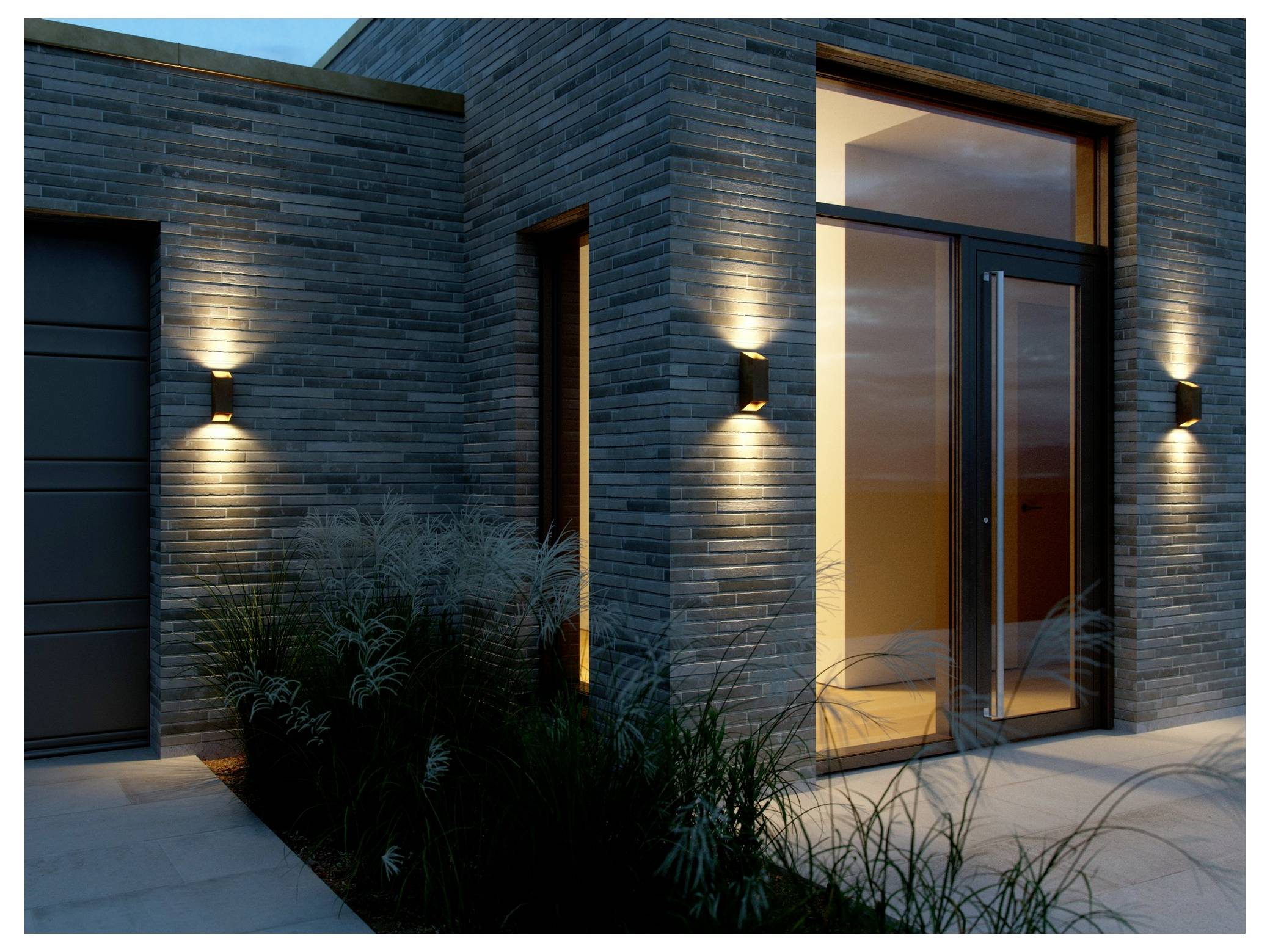 Eine moderne Gebäudefassade mit beleuchteten Ziegelmauern und einer Glastür. Dekorative Beleuchtung wirft nach oben strahlende Lichteffekte, die den Eingang hervorheben.