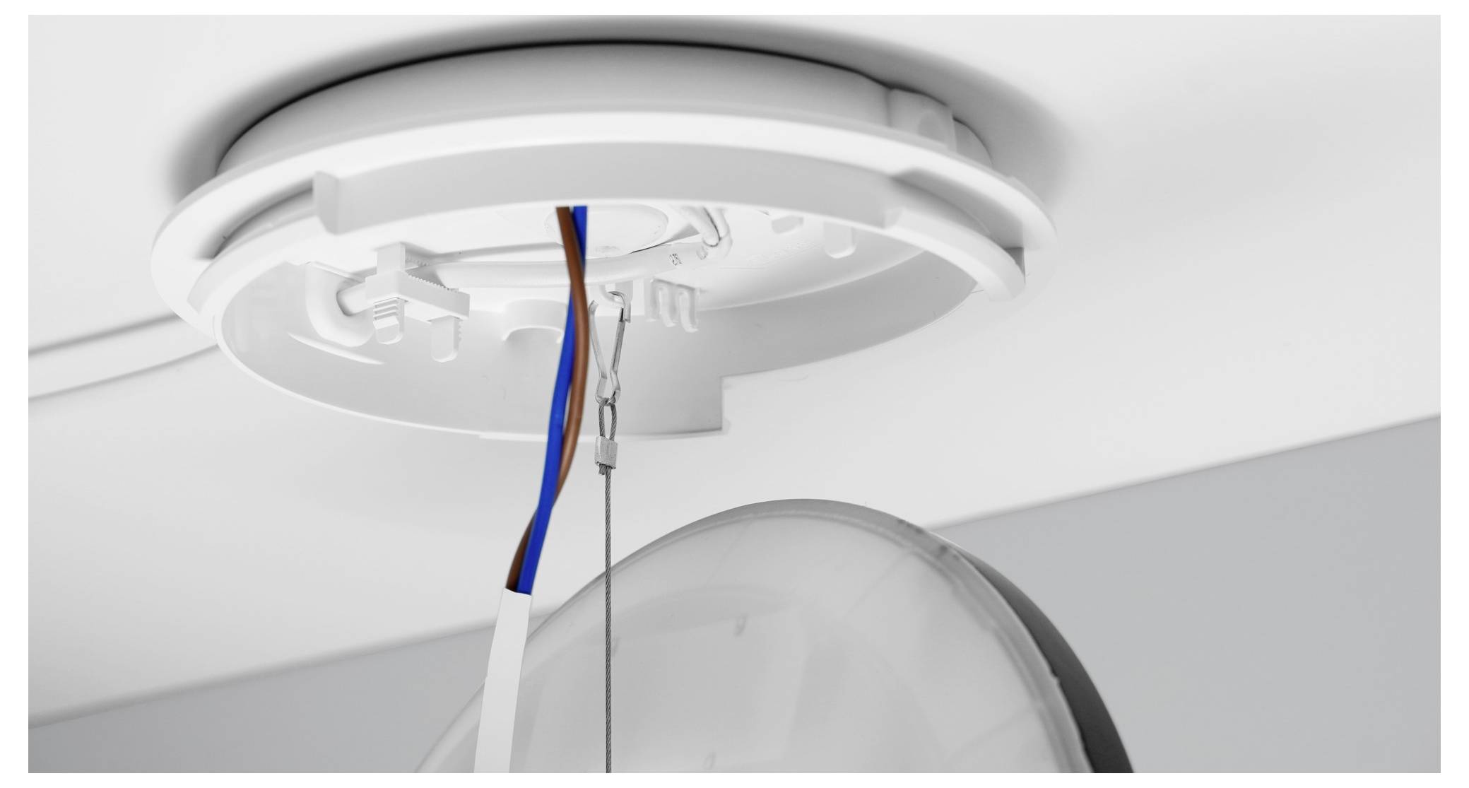 Eine runde Deckenleuchte wird installiert, wobei freigelegte Drähte sichtbar sind. Die Decke und eine weiße Basis für die Leuchte werden gezeigt.
