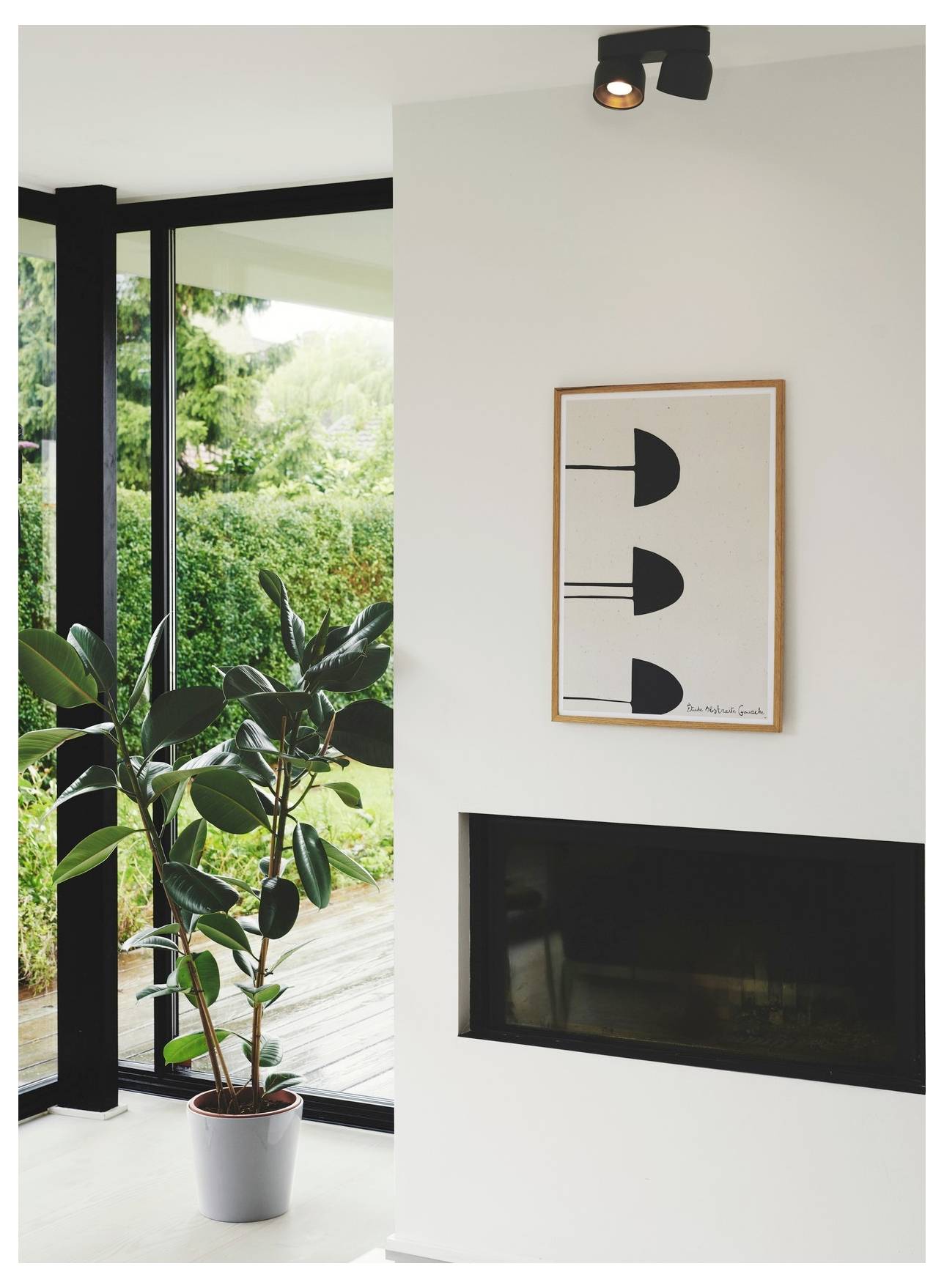 Ein moderner Wohnraum mit großen Fenstern, einer Topfpflanze am Fenster und einem minimalistischen gerahmten Kunstwerk über einem eleganten Kamin.