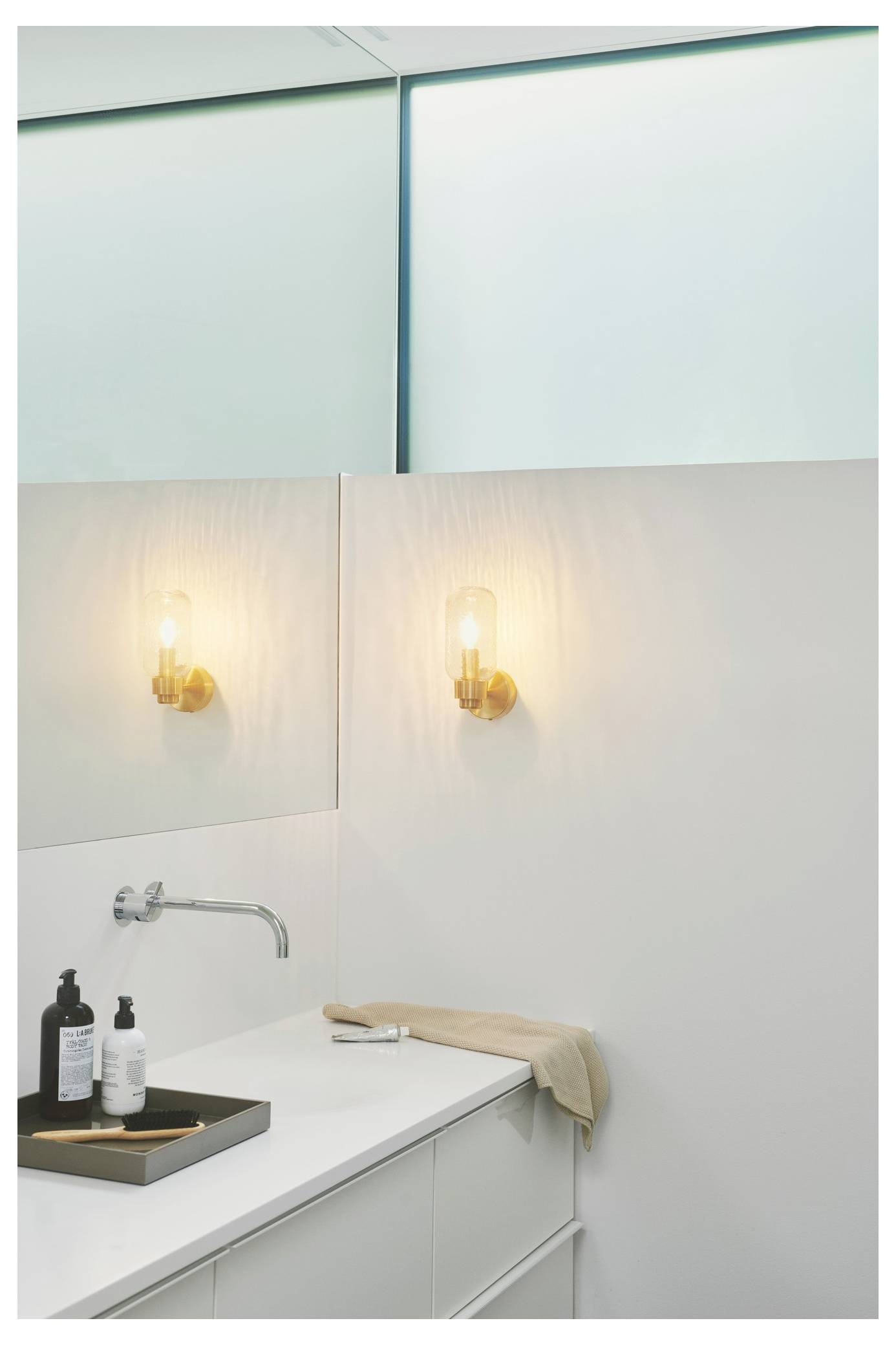 Ein modernes Badezimmer mit einem eleganten Waschbecken, beleuchtet durch ein warmes Wandlicht. Ein Handtuch und ein Seifenspender sind auf der Arbeitsplatte platziert.