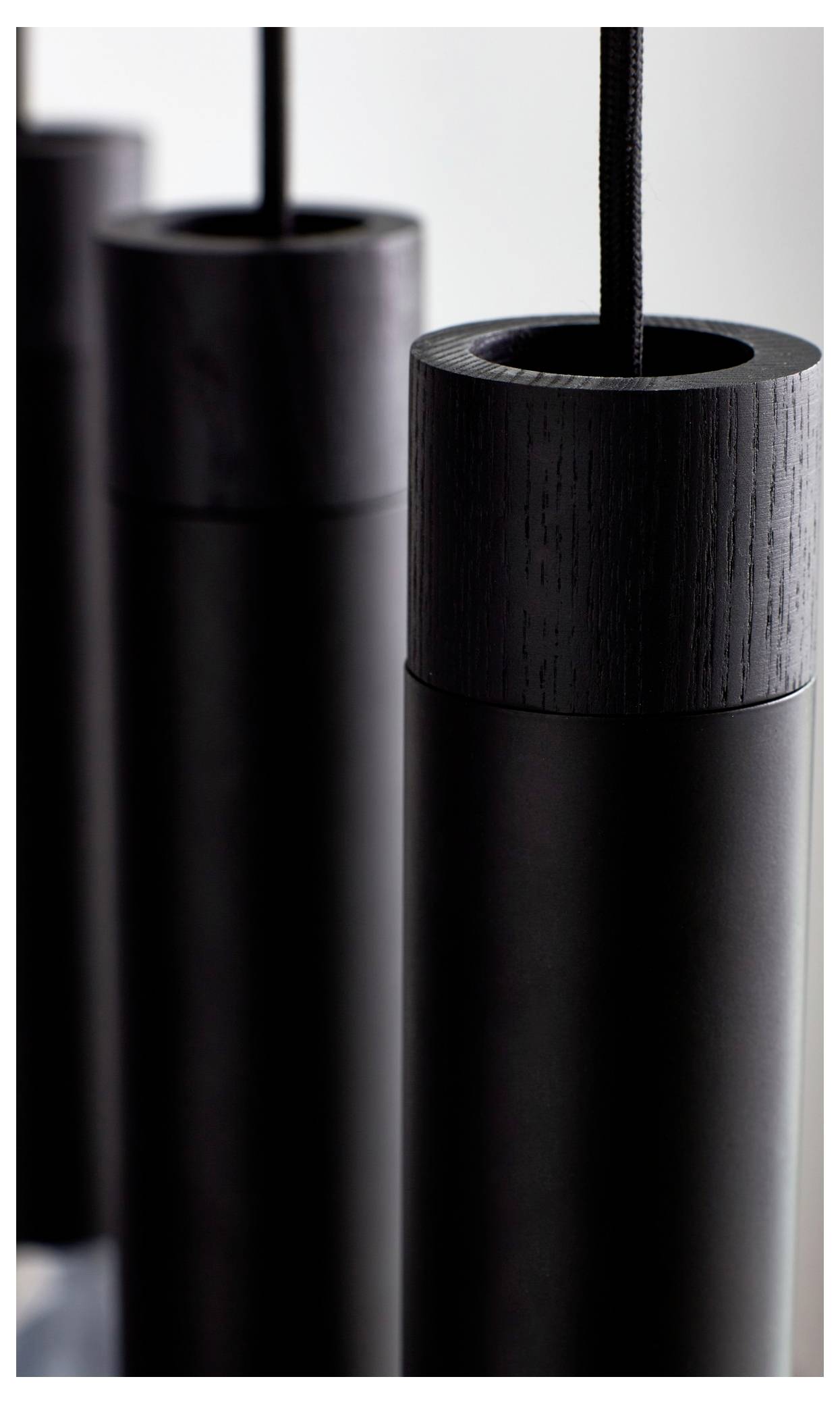 Nahaufnahme von drei modernen zylindrischen Pendelleuchten in dunklem Finish, die ein minimalistisches Design mit Kabeln zeigen, die von oben herunterhängen.