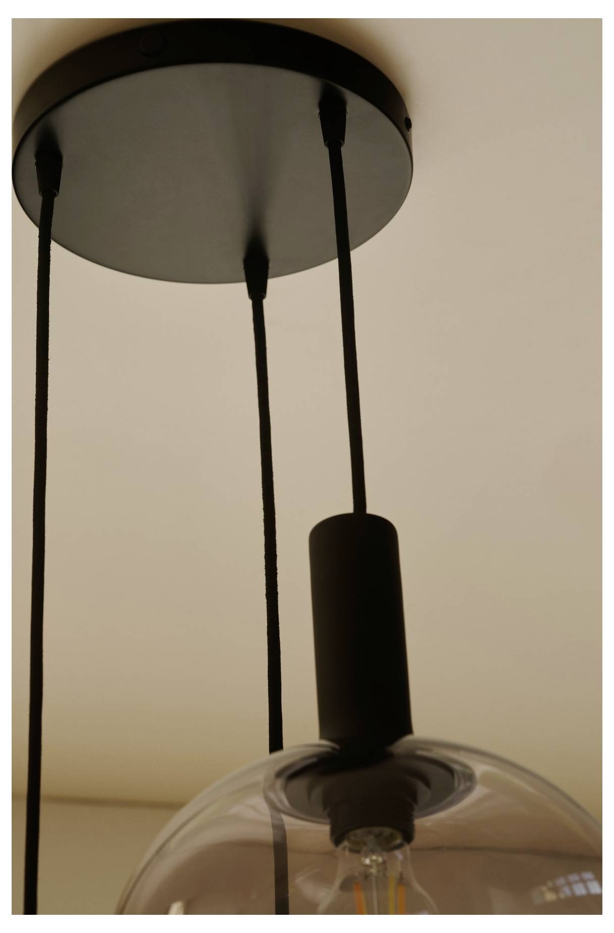 Eine runde schwarze Deckenleuchte mit zwei schwarzen Schnüren, die eine klare Glühbirne aufhängen, montiert an einer hellen Decke.