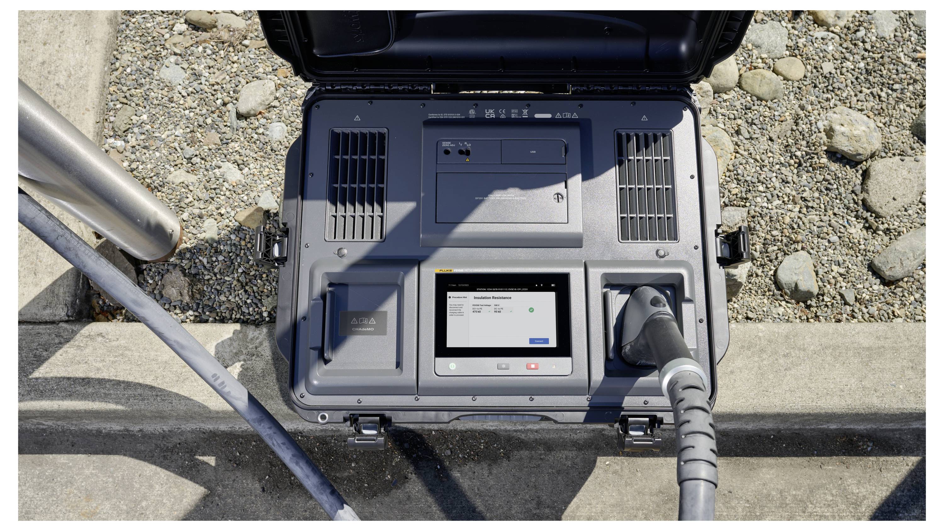 Eine tragbare Elektroladestation mit angeschlossenem Kabel und digitaler Anzeige, die den Ladestatus anzeigt, auf felsigem Untergrund positioniert.