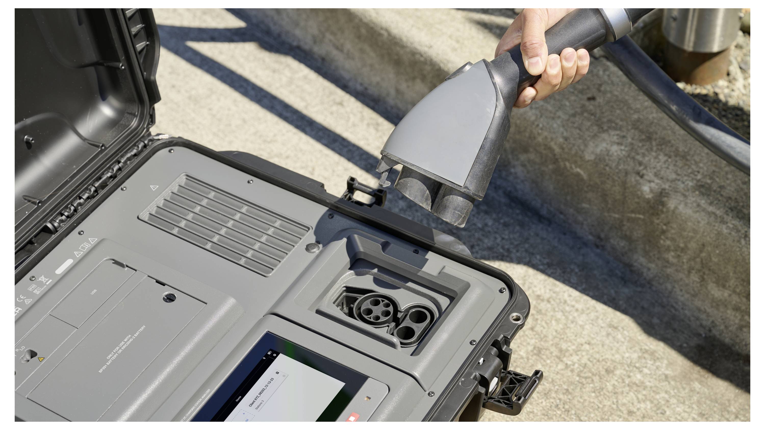 Eine Hand steckt ein Elektrofahrzeug-Ladegerät (EV-Ladegerät) in eine Ladebuchse einer Stromversorgungseinheit, was auf das Laden von Elektrofahrzeugen hinweist.