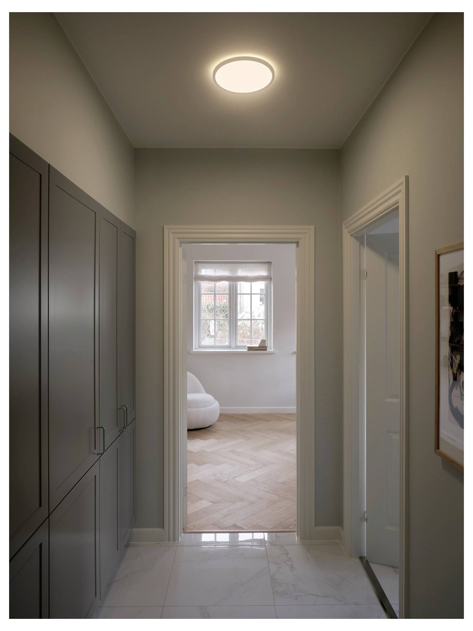 Ein enger Flur mit Schränken auf der linken Seite öffnet sich zu einem gemütlichen, hellen Raum mit Parkettboden und einem großen Fenster.