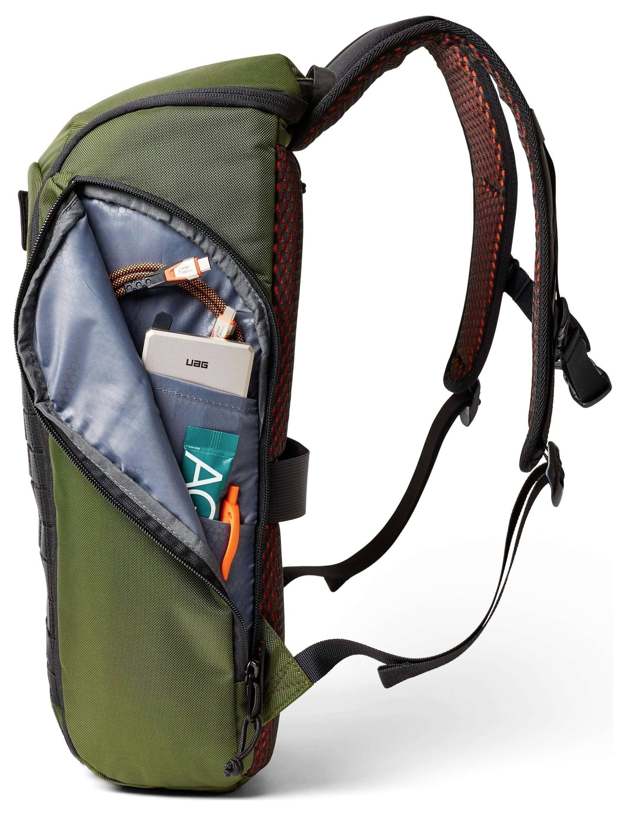 Ein grüner Rucksack mit einer offenen Seitentasche, in der eine USB-Powerbank, ein aufgerolltes oranges Kabel und ein kleiner persönlicher Gegenstand zu sehen sind.