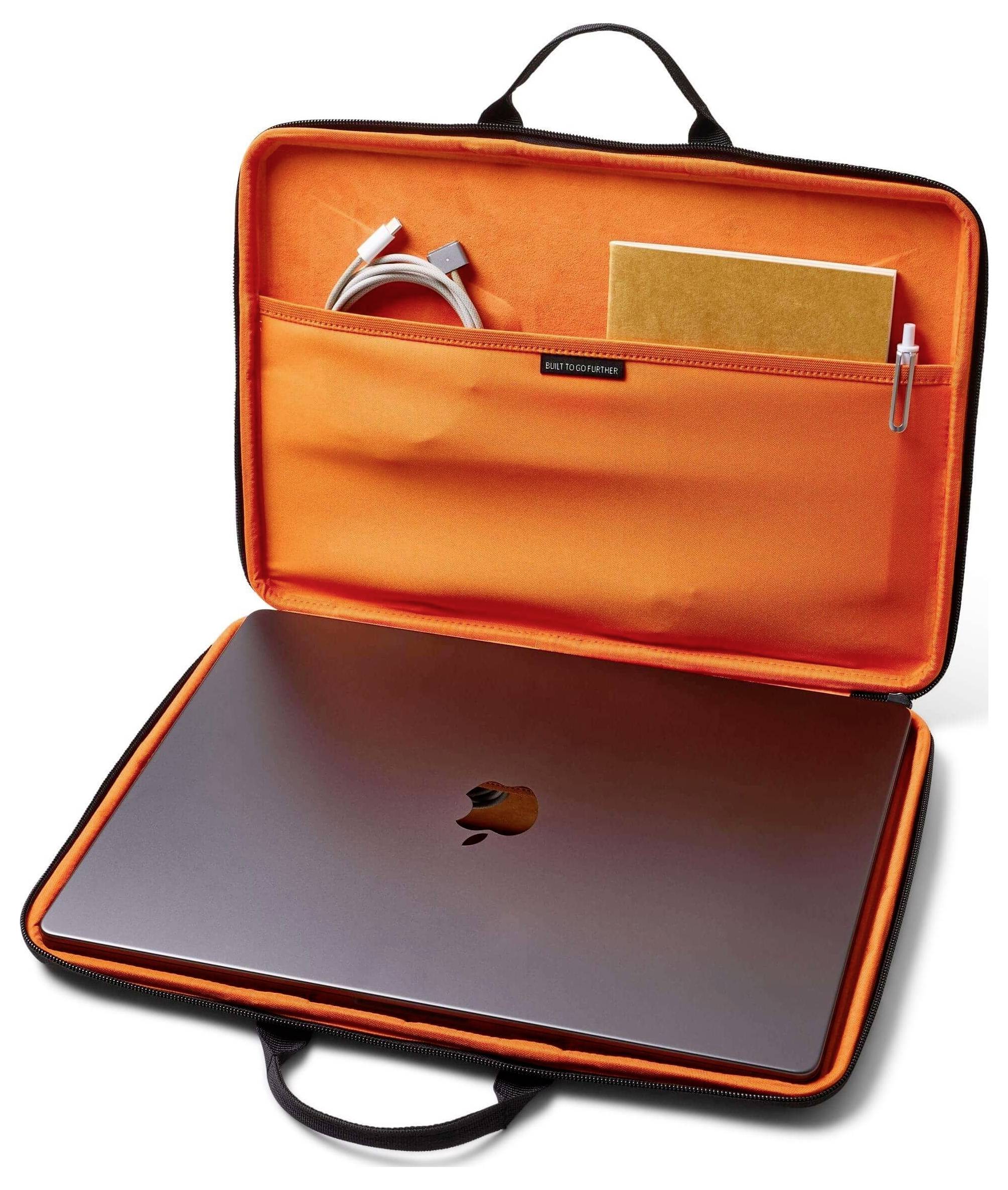 Ein offenes orangefarbenes Laptoptasche zeigt einen geschlossenen Laptop, ein aufgerolltes Kabel, ein Notizbuch und einen Stift, alle ordentlich in Taschen organisiert.