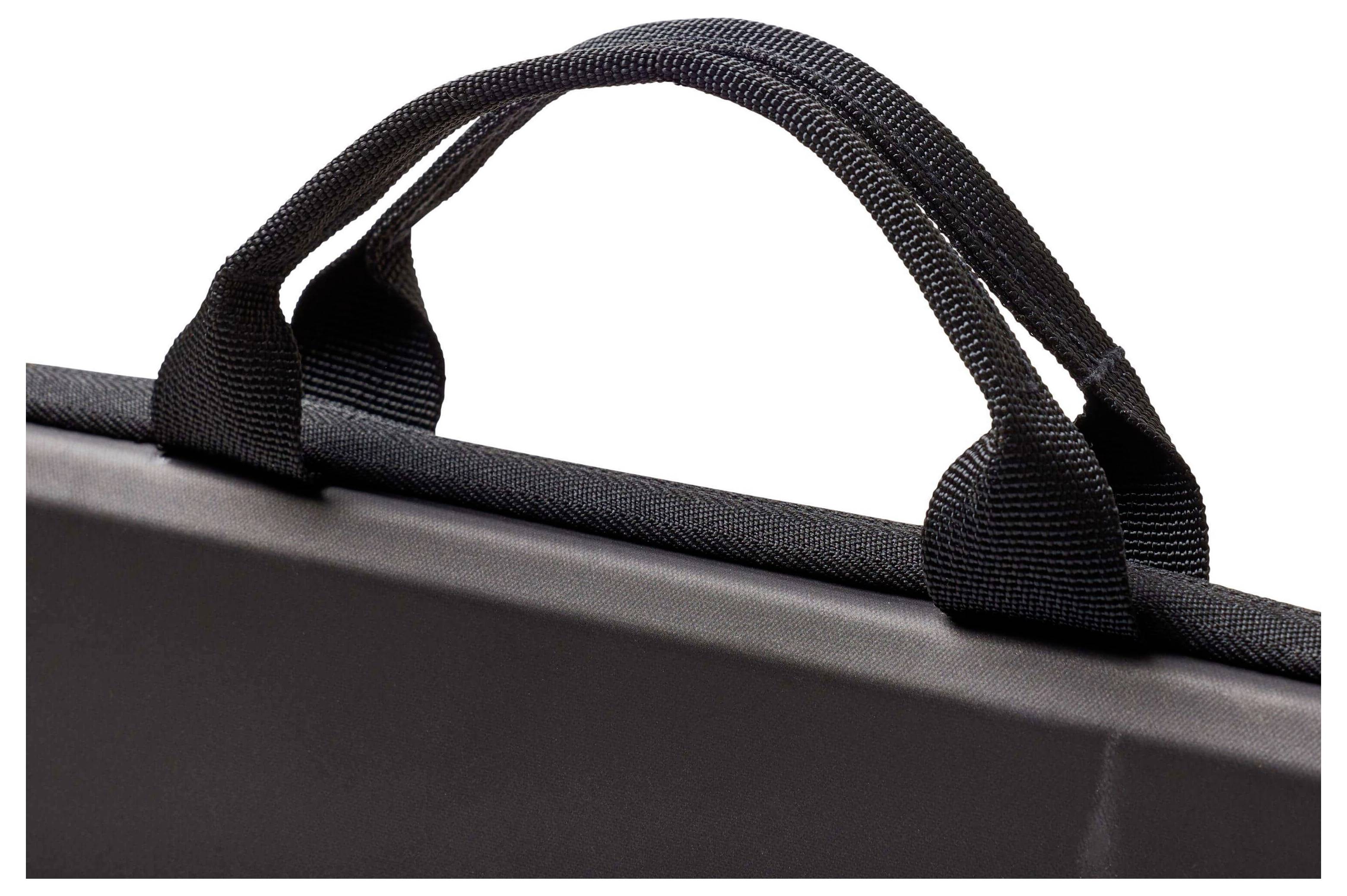 Eine Nahaufnahme eines schwarzen Stoffgriffs an einem hartschaligen Koffer oder einer Tasche, die die Textur und Nähdetails zeigt.