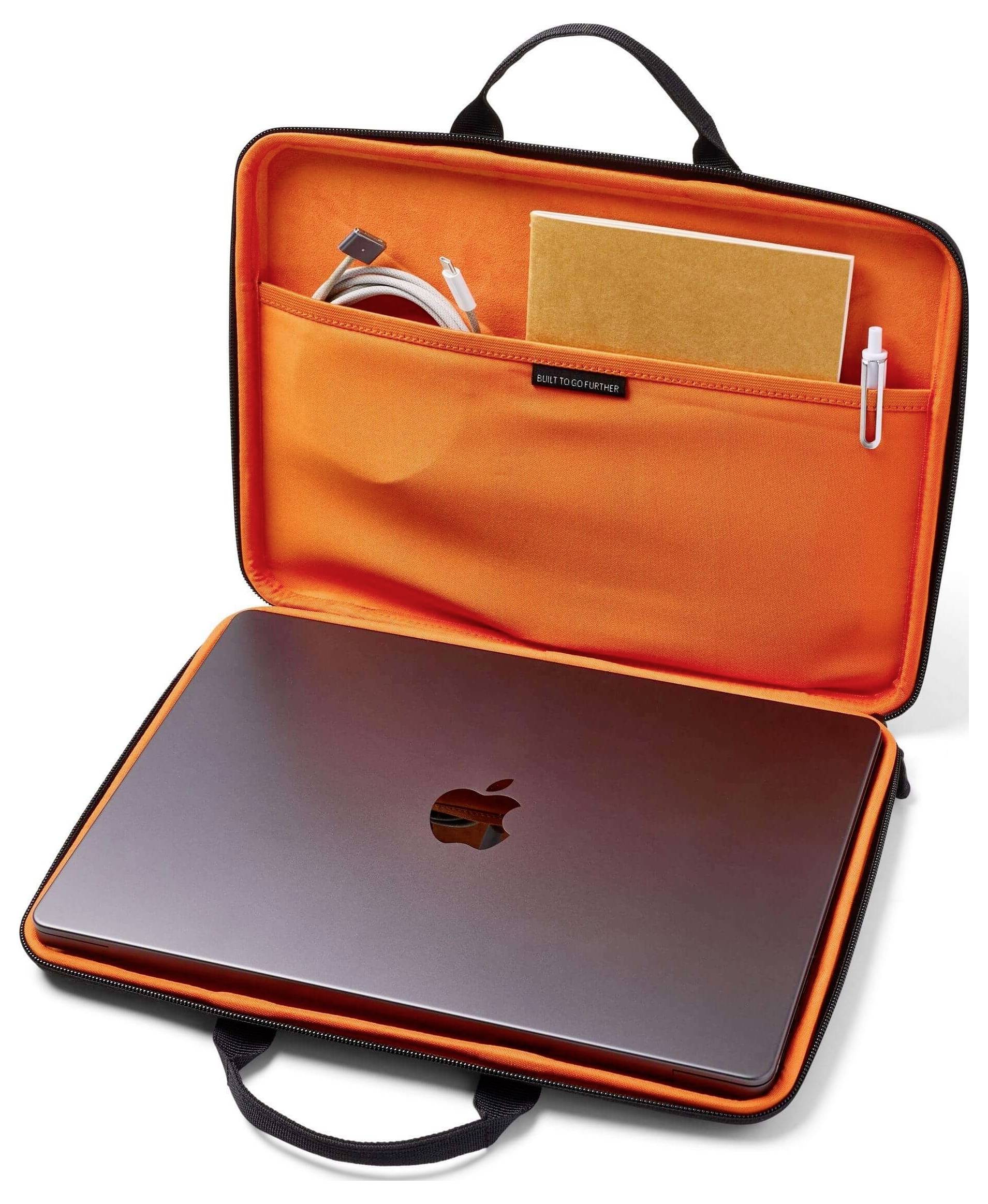 Offener Laptop-Koffer mit orangefarbenem Inneren, enthaltend einen silbernen Laptop, ein Notizbuch, einen Stift und ein aufgerolltes Kabel in der Tasche.