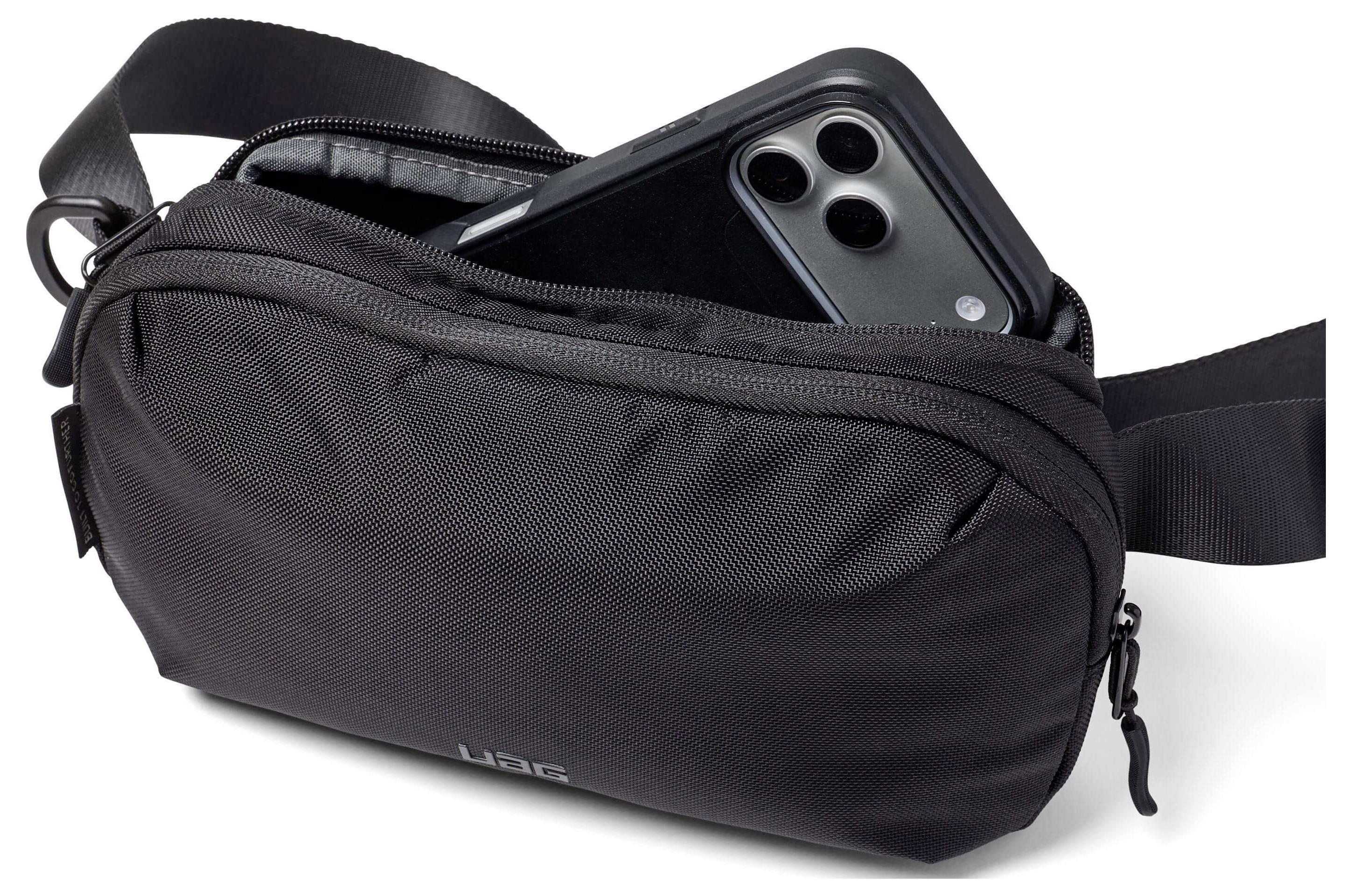 Eine schwarze Umhängetasche mit teilweise geöffnetem Reißverschluss, der ein Smartphone im Inneren zeigt, demonstriert die Speicherkapazität der Tasche.