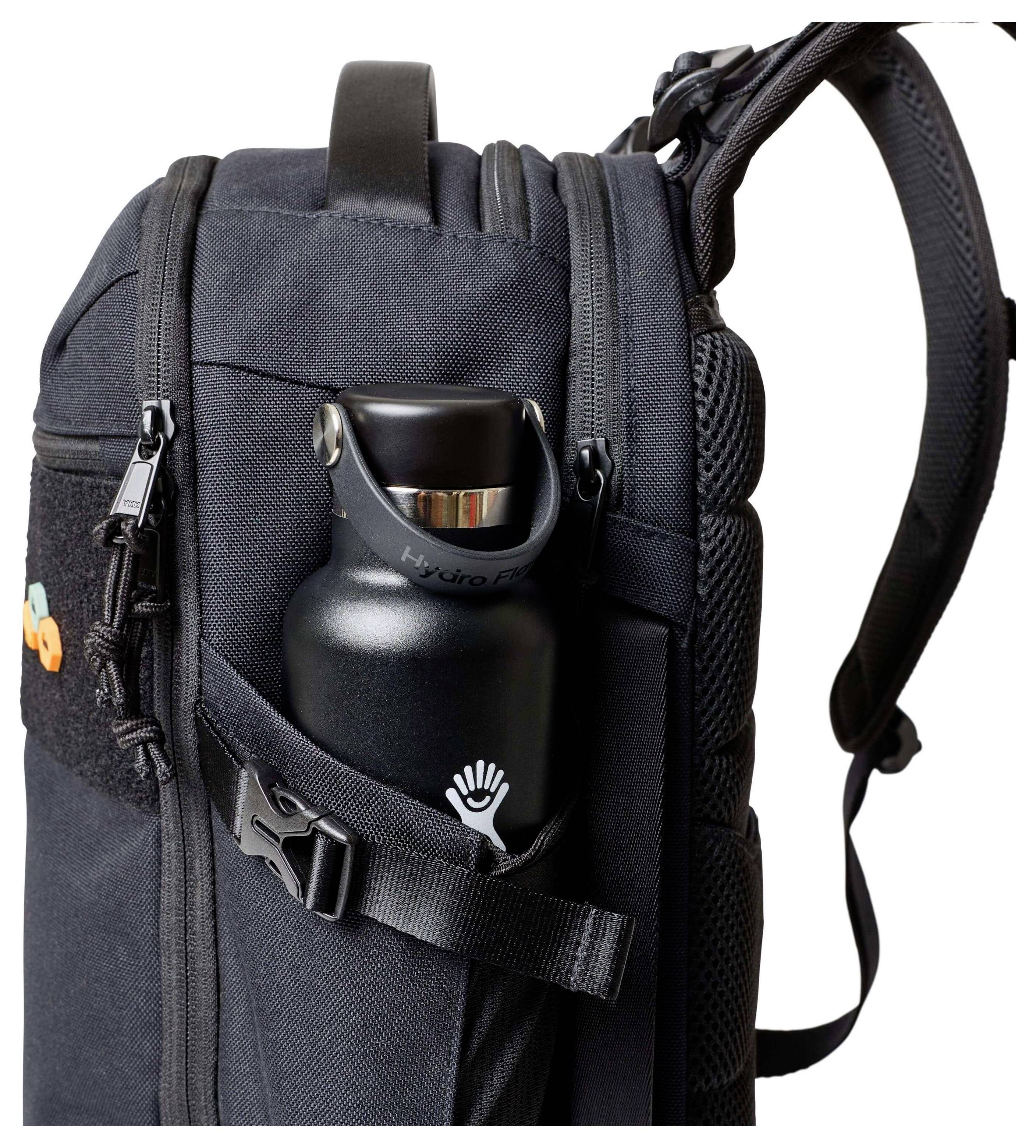 Ein schwarzer Rucksack mit mehreren Fächern, in dem eine Wasserflasche in einer Seitentasche steckt und durch einen Riemen gesichert wird.