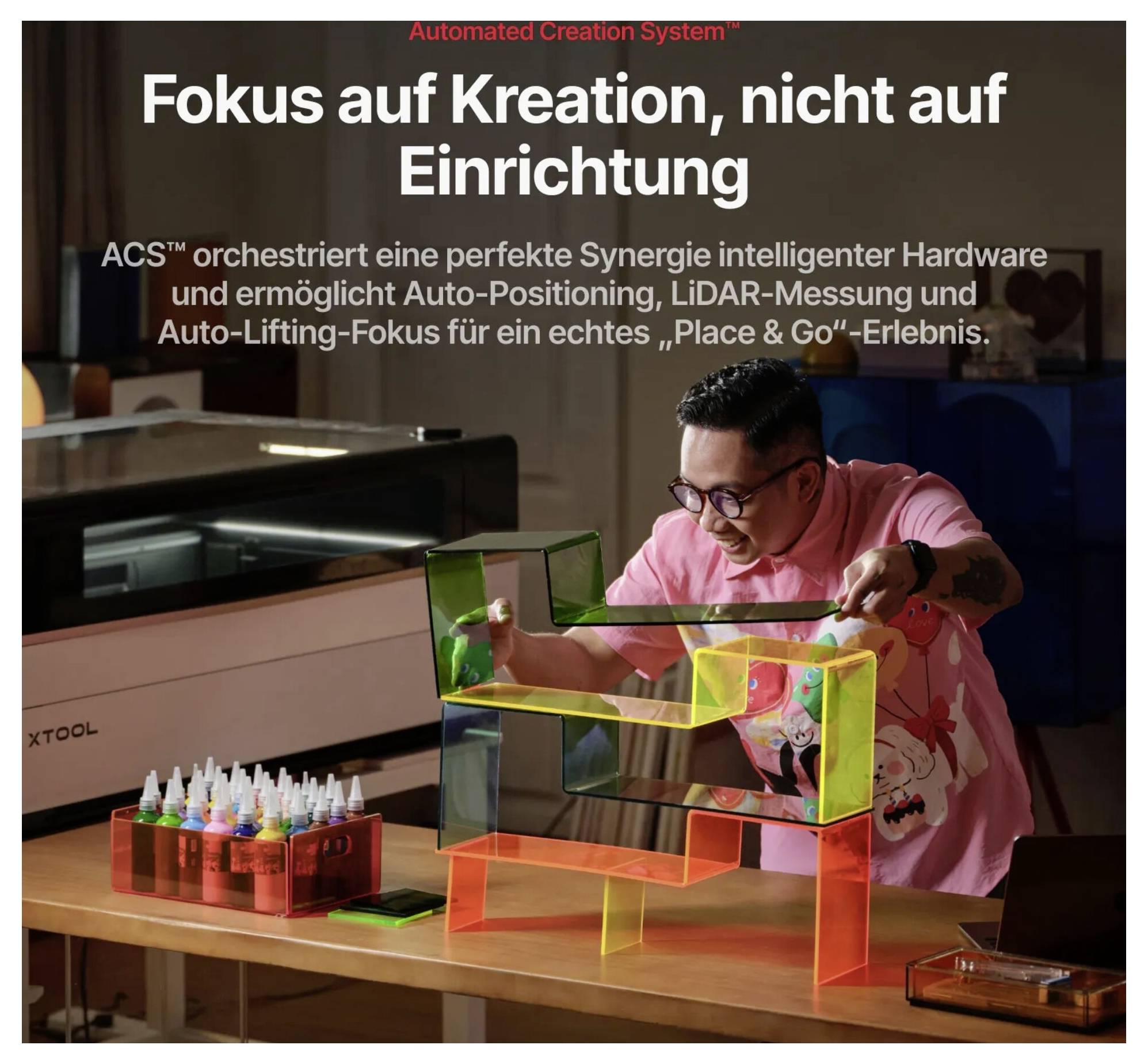 Ein Mann stellt eine leuchtende Acryl-Anordnung neben einer xTool-Maschine ein; deutscher Text sagt „Konzentriere dich auf die Kreation, nicht auf die Einrichtung