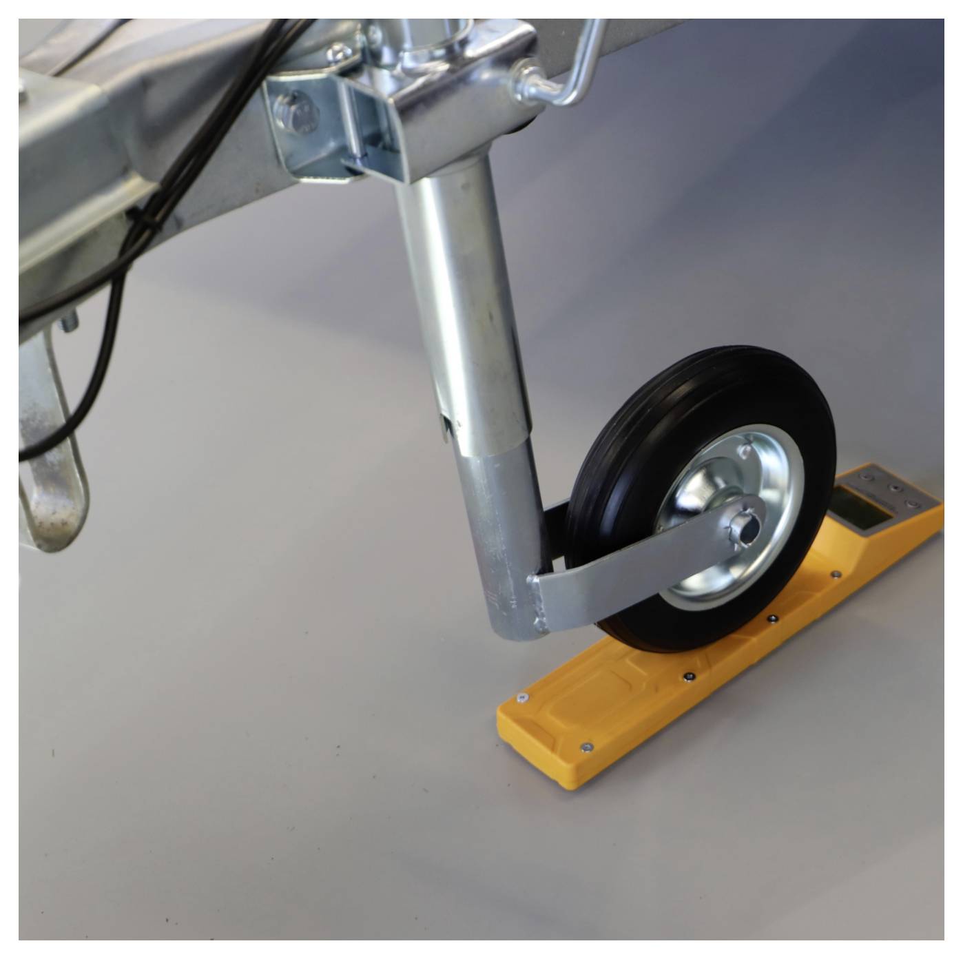 Ein Anhängerwagenheberrad, das auf einem gelben Radkeil gesichert ist und eine Bewegung auf einer glatten grauen Oberfläche verhindert.