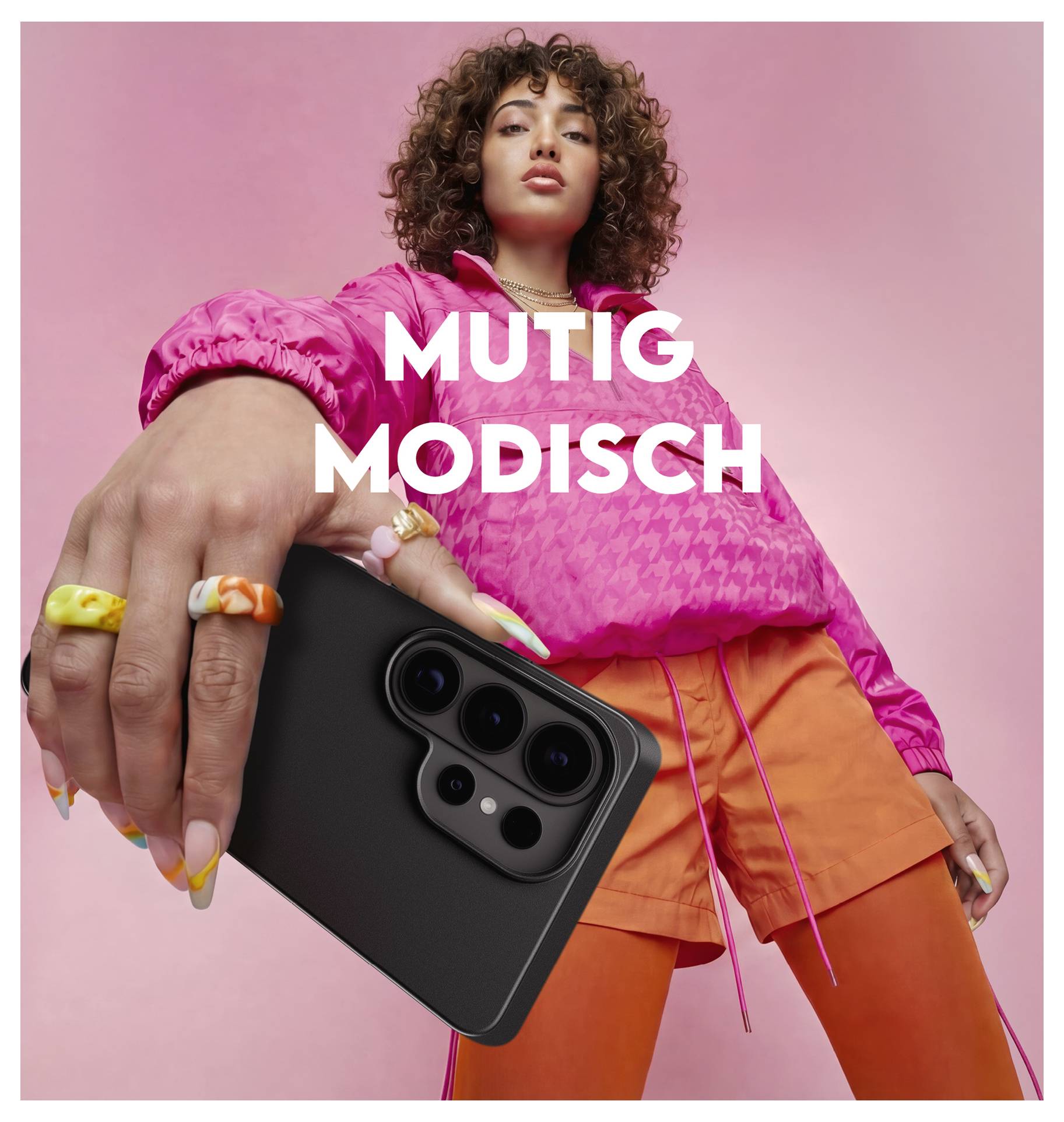 Eine Person in bunter Mode hält ein Smartphone und richtet es auf den Betrachter. Der Text „MUTIG MODISCH
